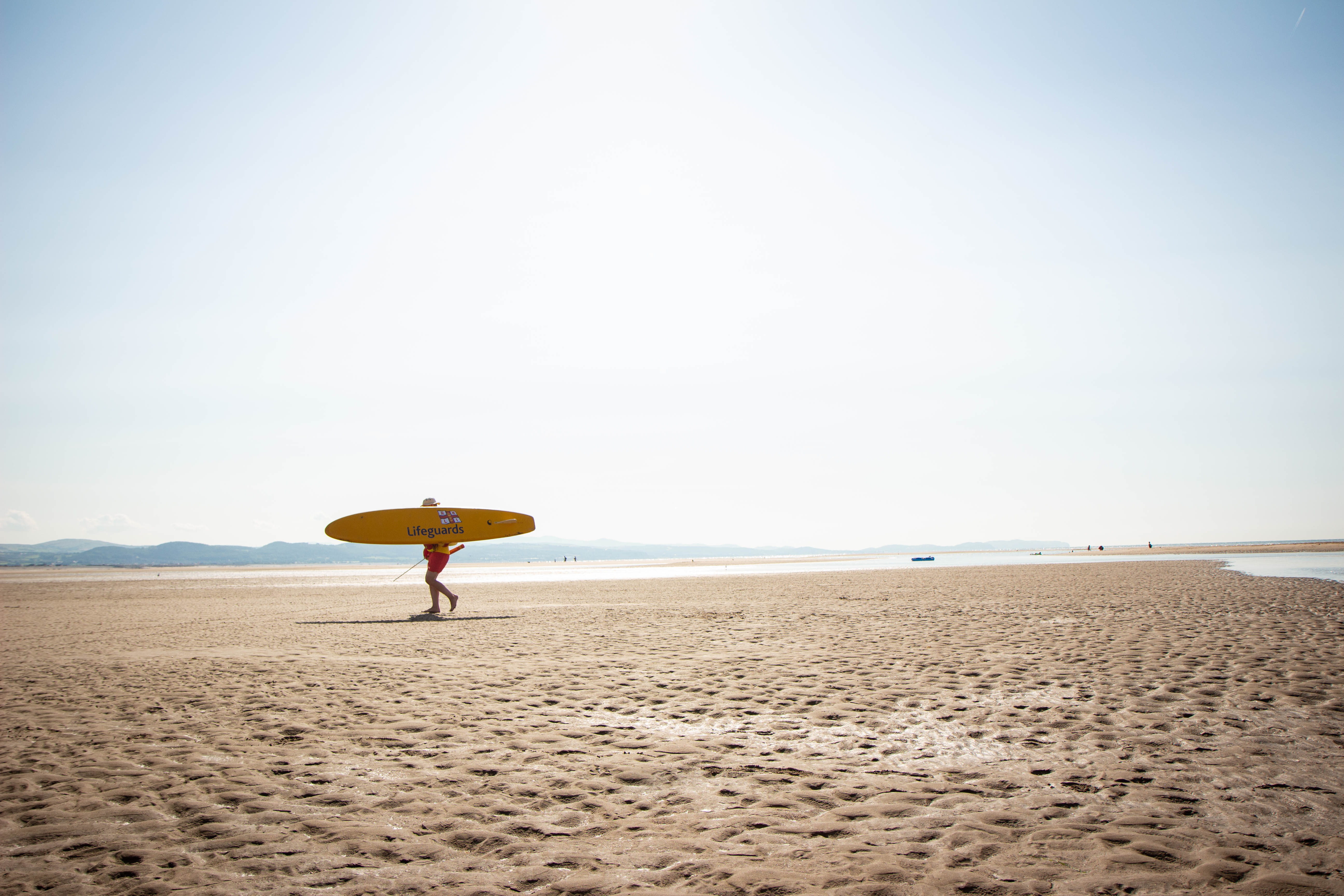 RNLI lifeguard walking on beach with rescue board 