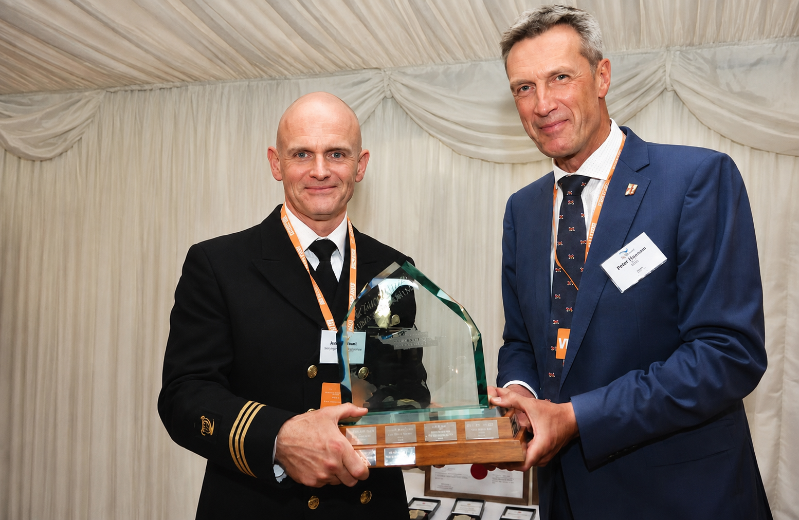 Winchamn James O'Neill receiving his trophy from Peter Sparkes, RNLI CEO, both facing and smiling to camera