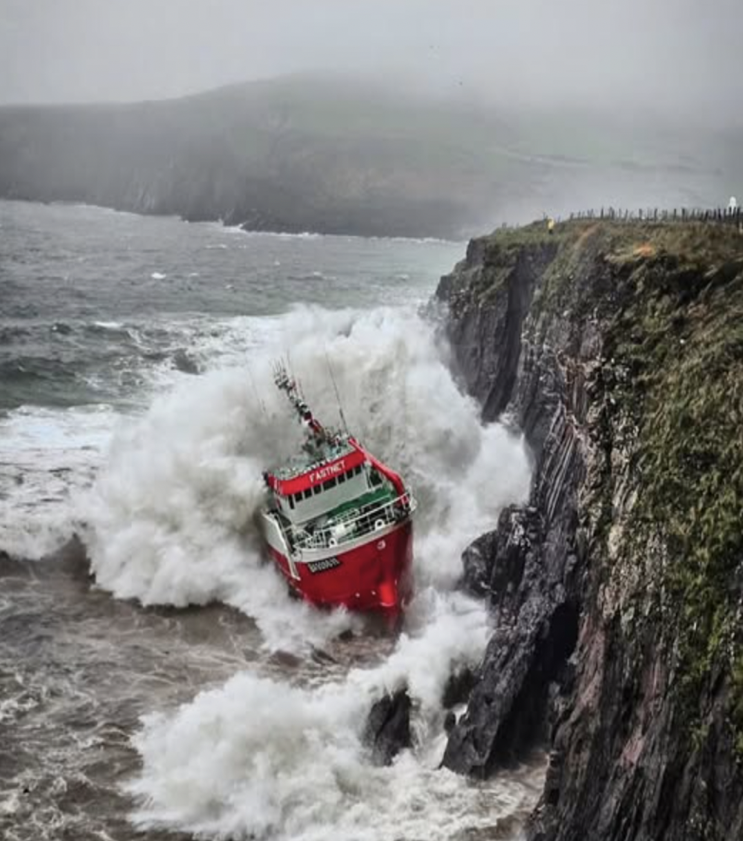 View of fishing vessel being pounded by the sea, aground at the bottom of cliffs near Dingle Harbour, Kerry, Ireland