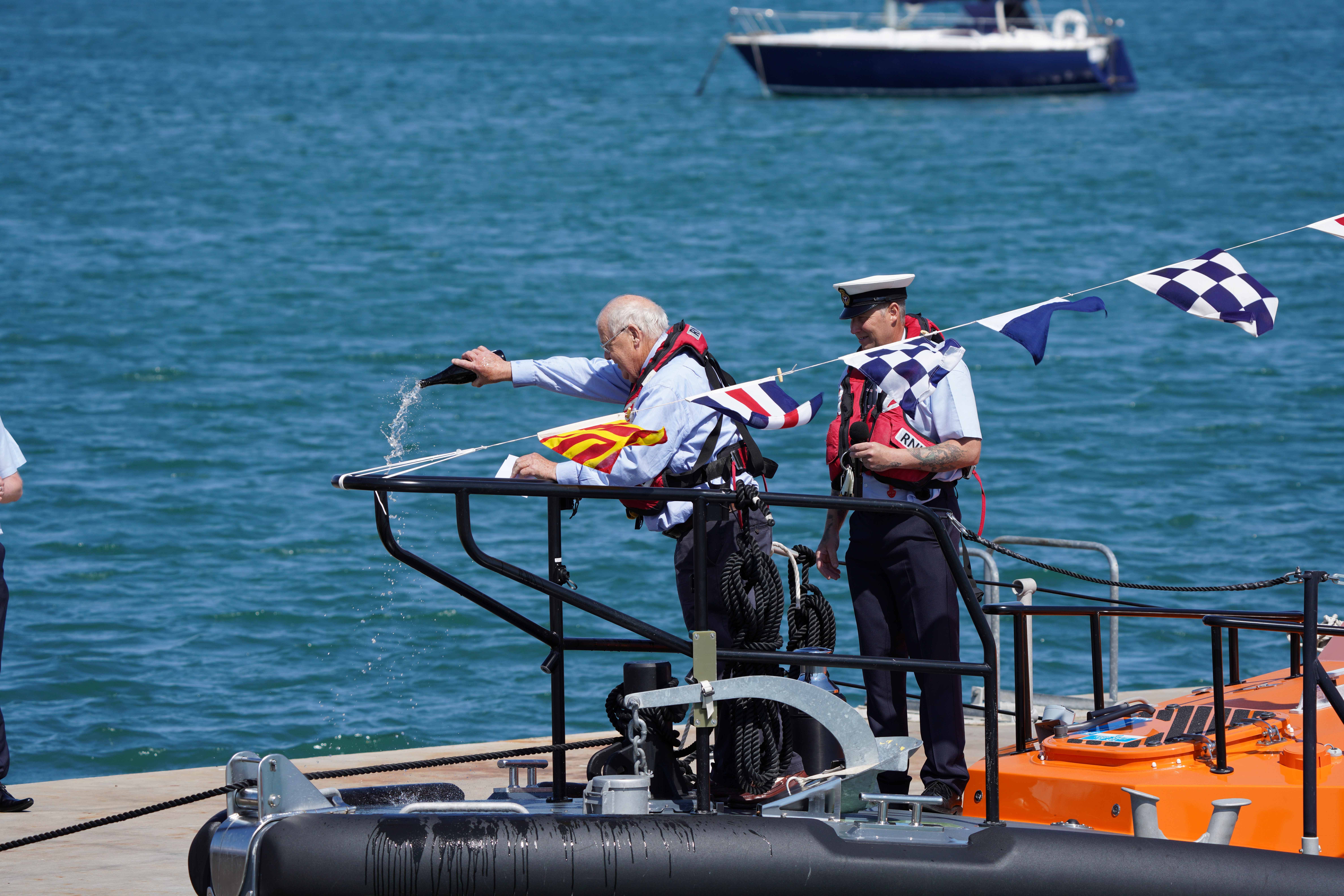Michael Cameron pouring a bottle of Saki over the lifeboat with Derek Rea looking on