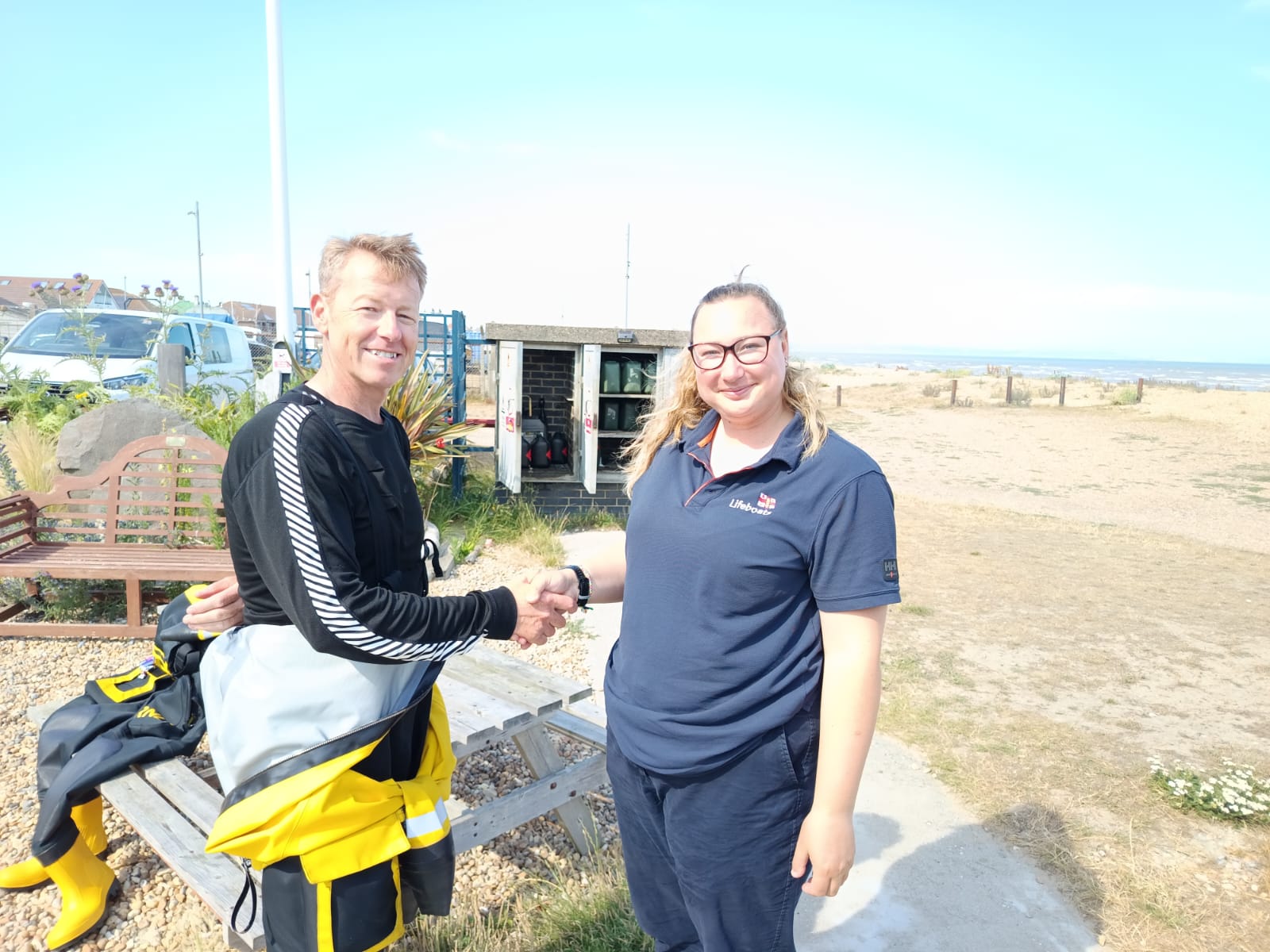 New helm Iain Anderson wearing yellow and black drysuit shakes hands with Coastal trainer Ruth Oliver