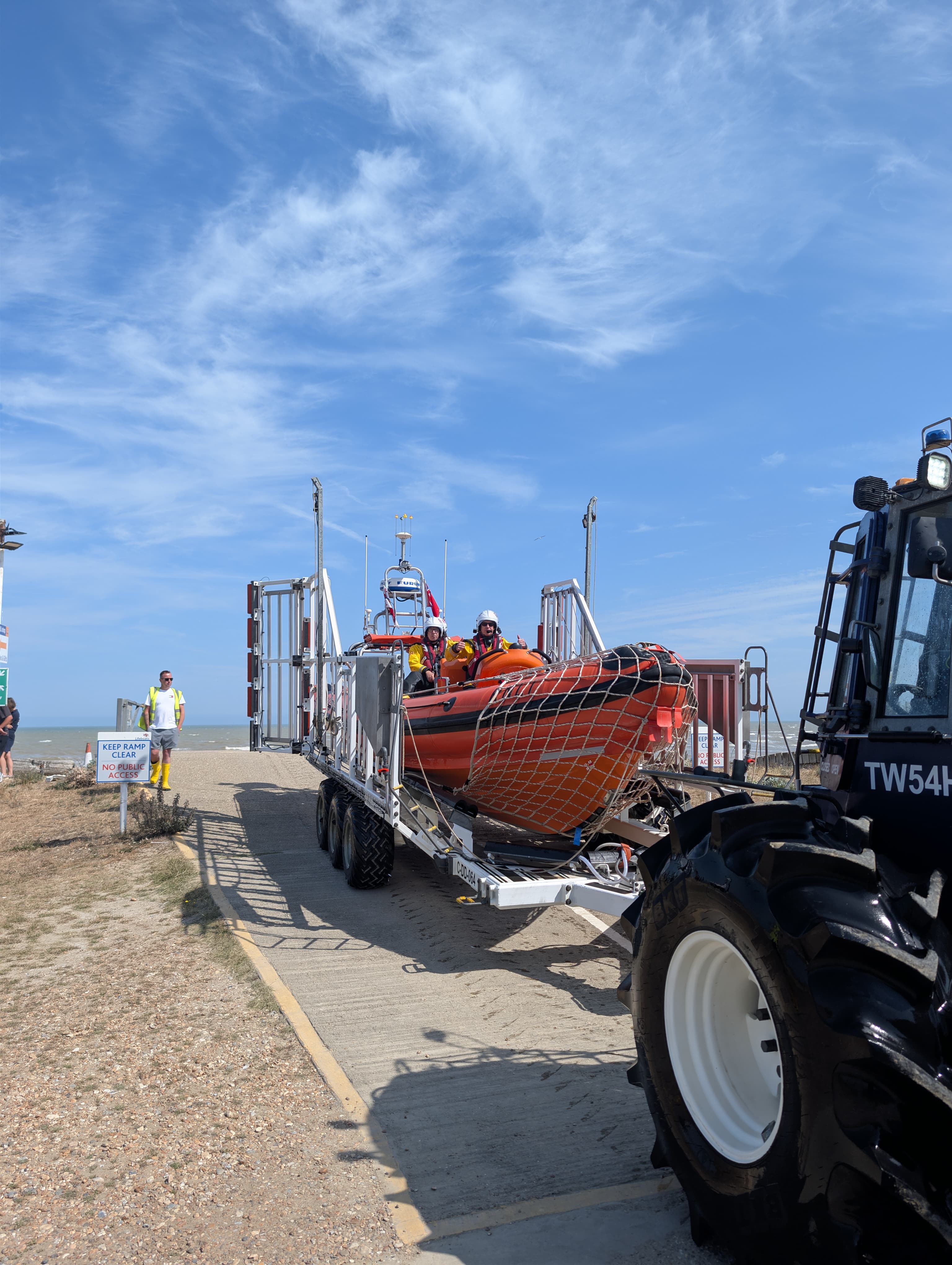 A large orange RNLI lifeboat with a blue sky behind it being brought back to the station post recovery