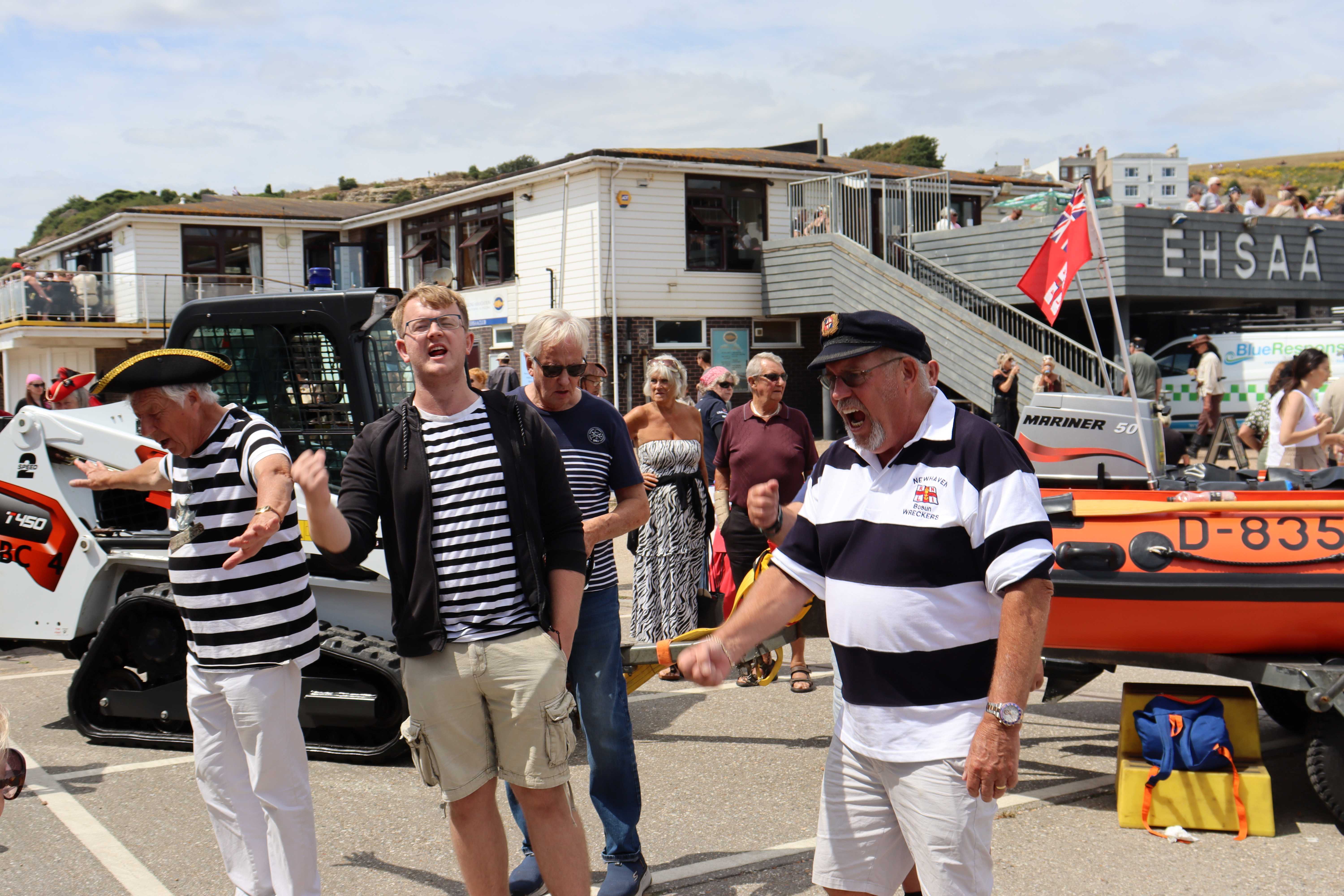 Shanty singers standing on the apron in front of an inshore lifeboat