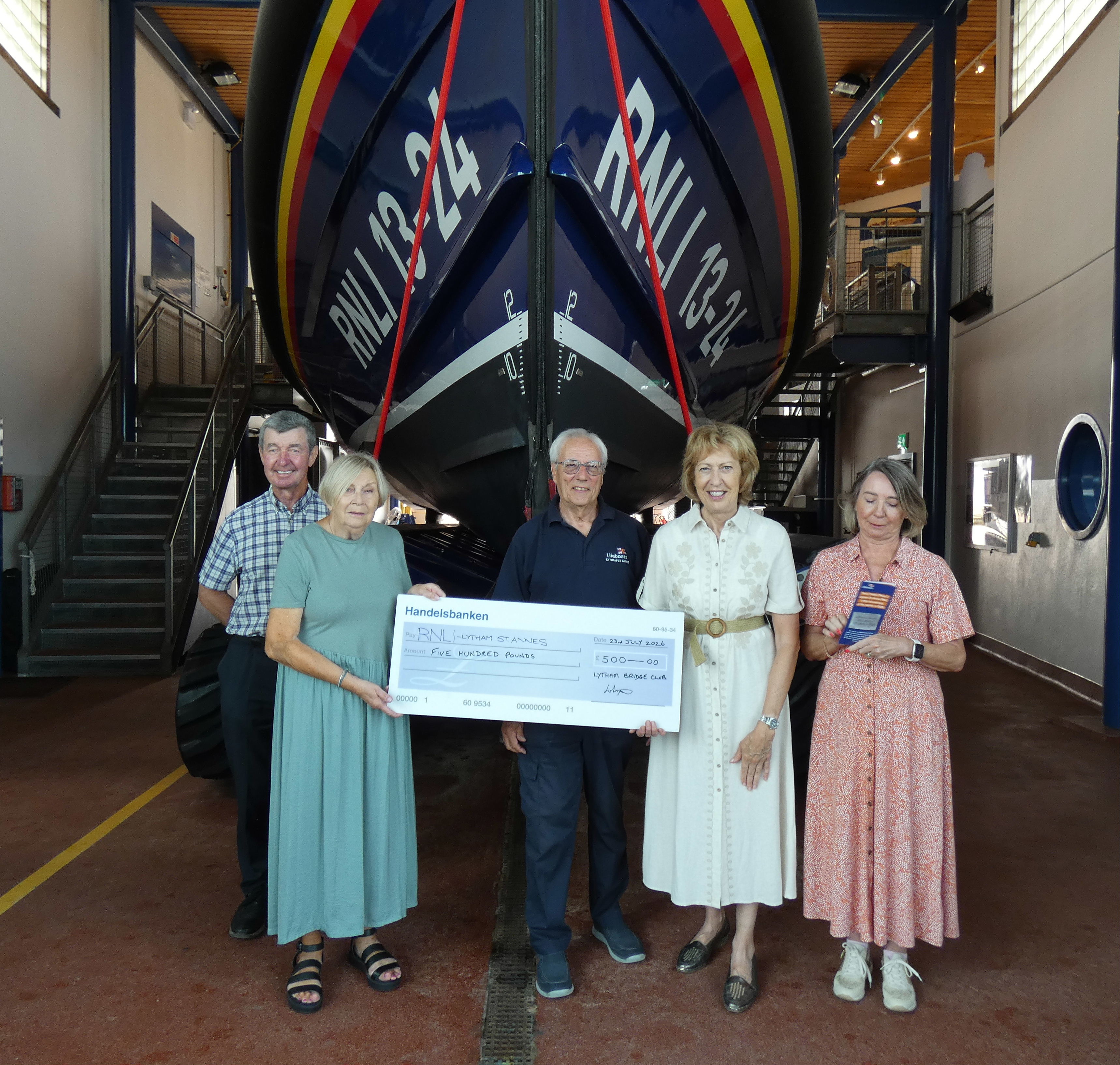 A group of people holding a large presentation cheque stand in front of a Lifeboat