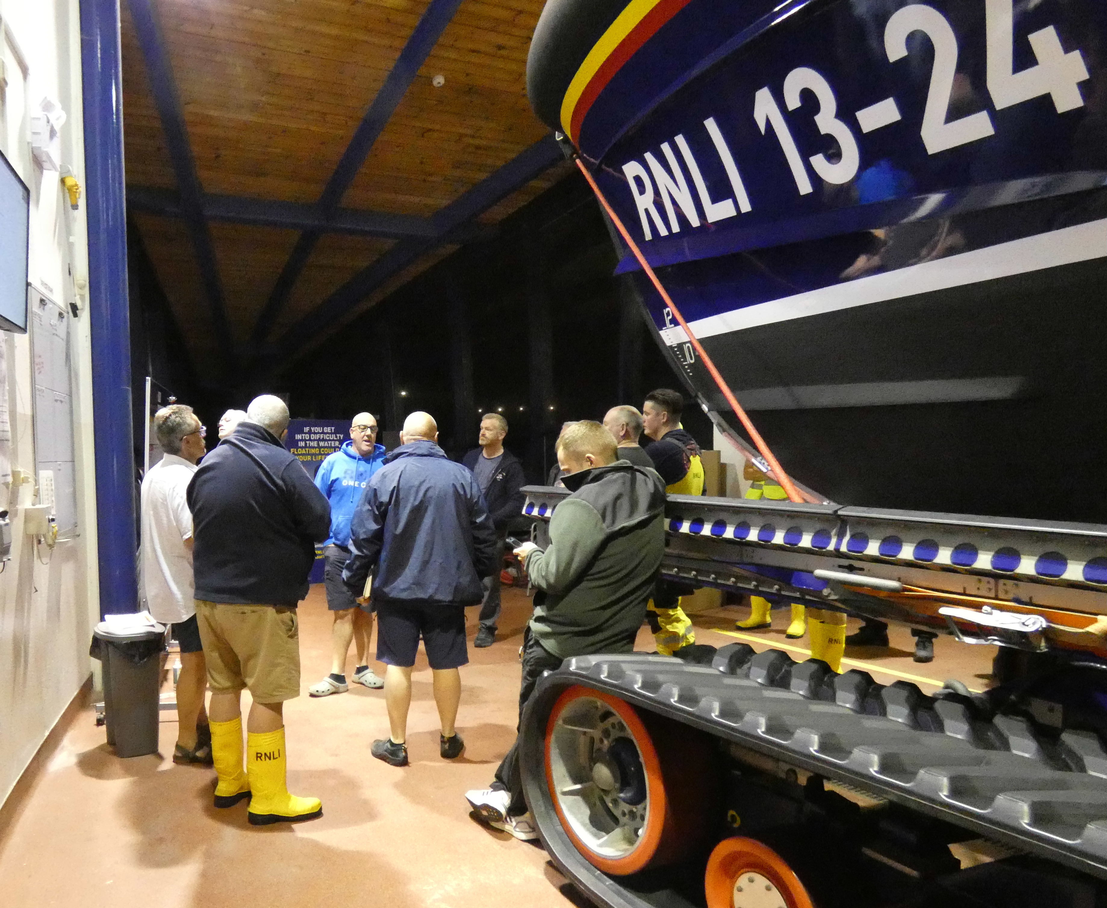 A group of men and women talk in front of a Lifeboat