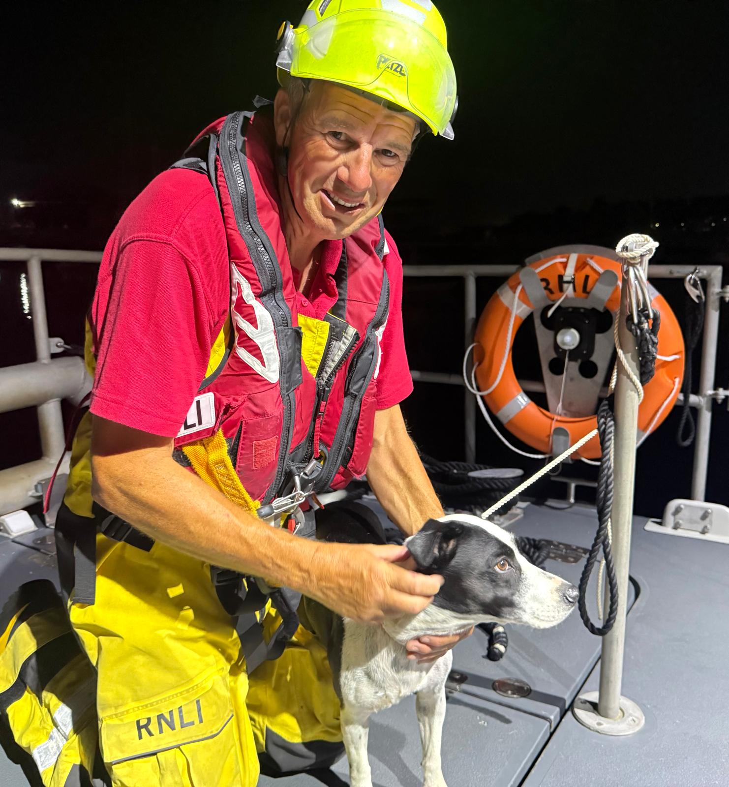 Crew member kneeling facing the camera comforting a black and white dog that was rescued