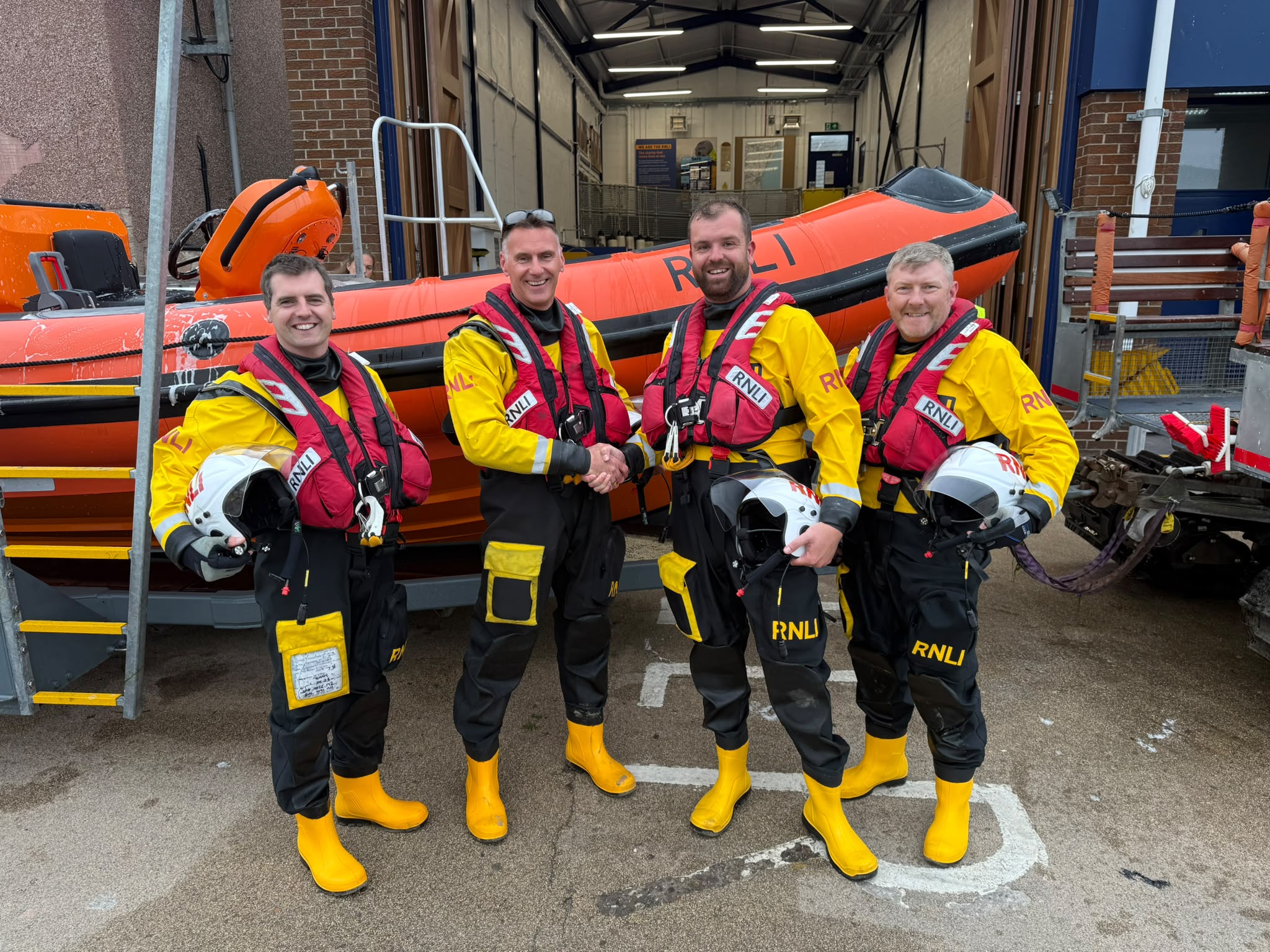 New helm shaking hands with RNLI area assessor stood in front of ILB with two other crew members.