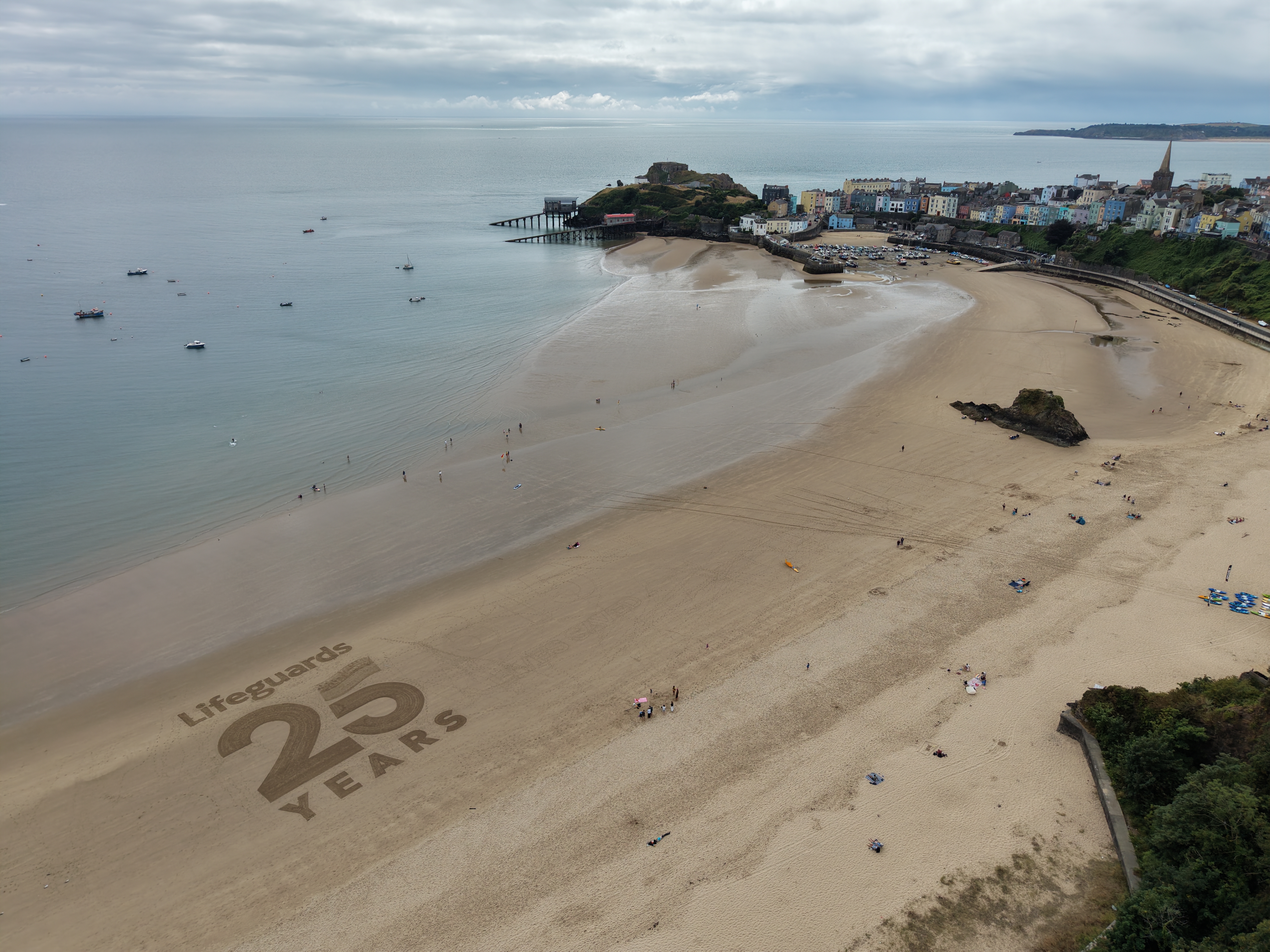 Image of a beach with Lifeguard 25 years sketched into the sand