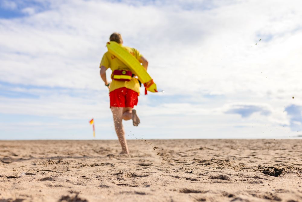 RNLI lifeguard in uniform running on the beach