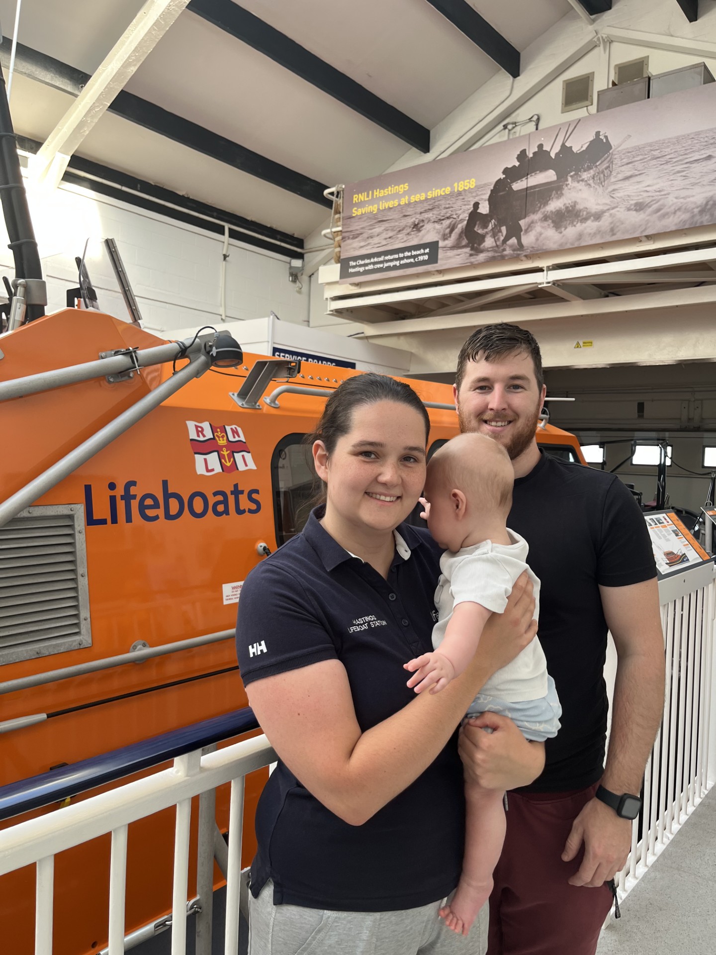 RNLI volunteer standing in front of lifeboat with partner and baby 