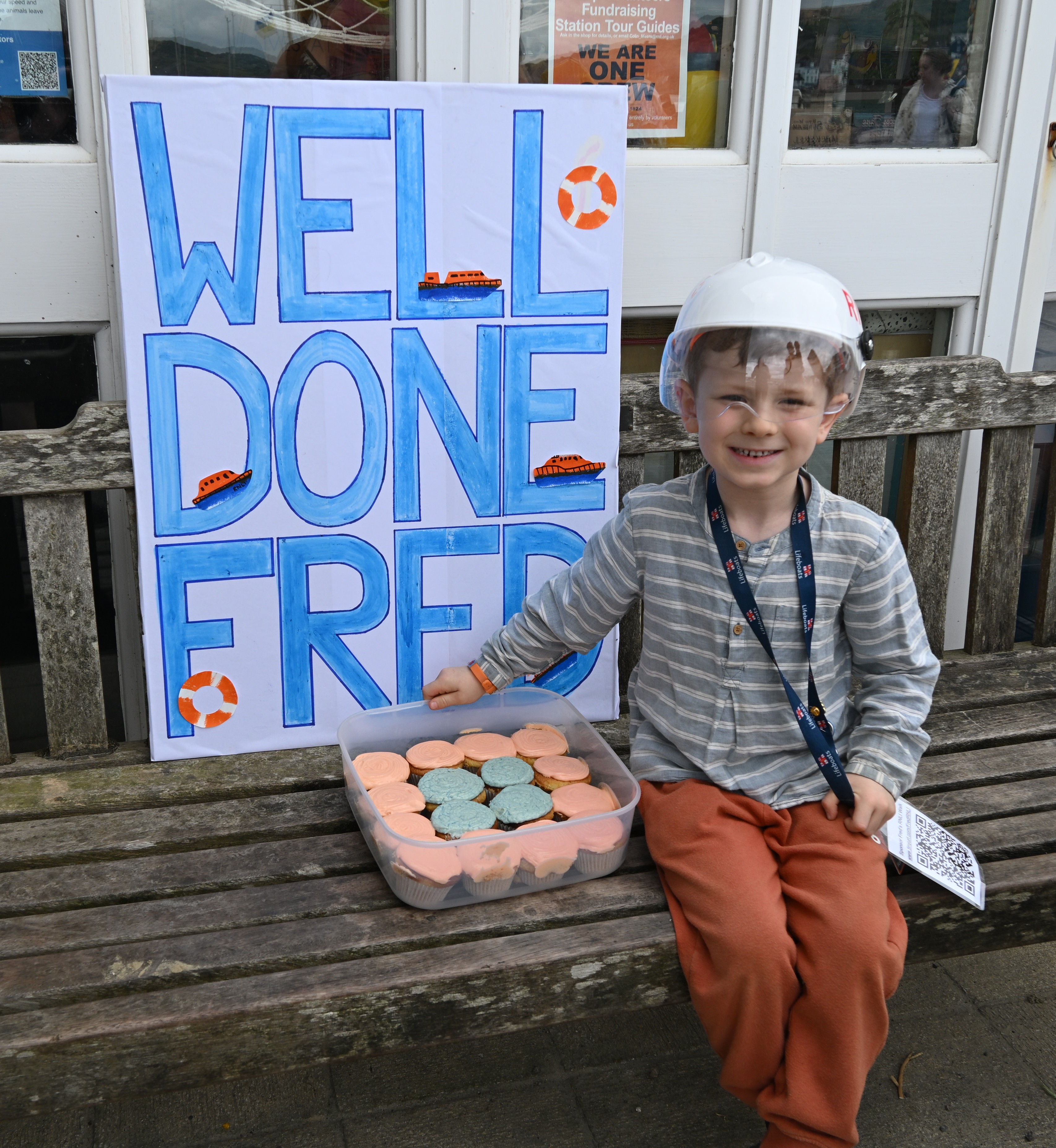 Boy with cakes in front of blue and white sign