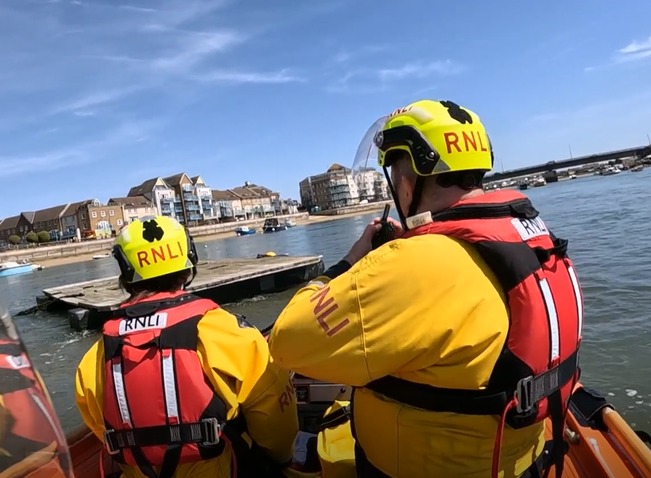Two RNLI crew are pictured from the back as they approach a pontoon on the River Adur. The casualty is not visible.