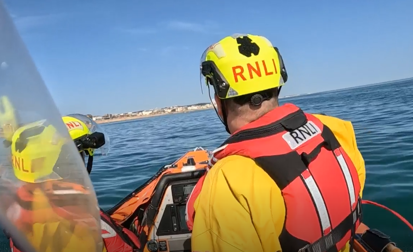 Two RNLI crew are pictured from the back on the inshore lifeboat off of Hove lawns. The casualty is not visible.