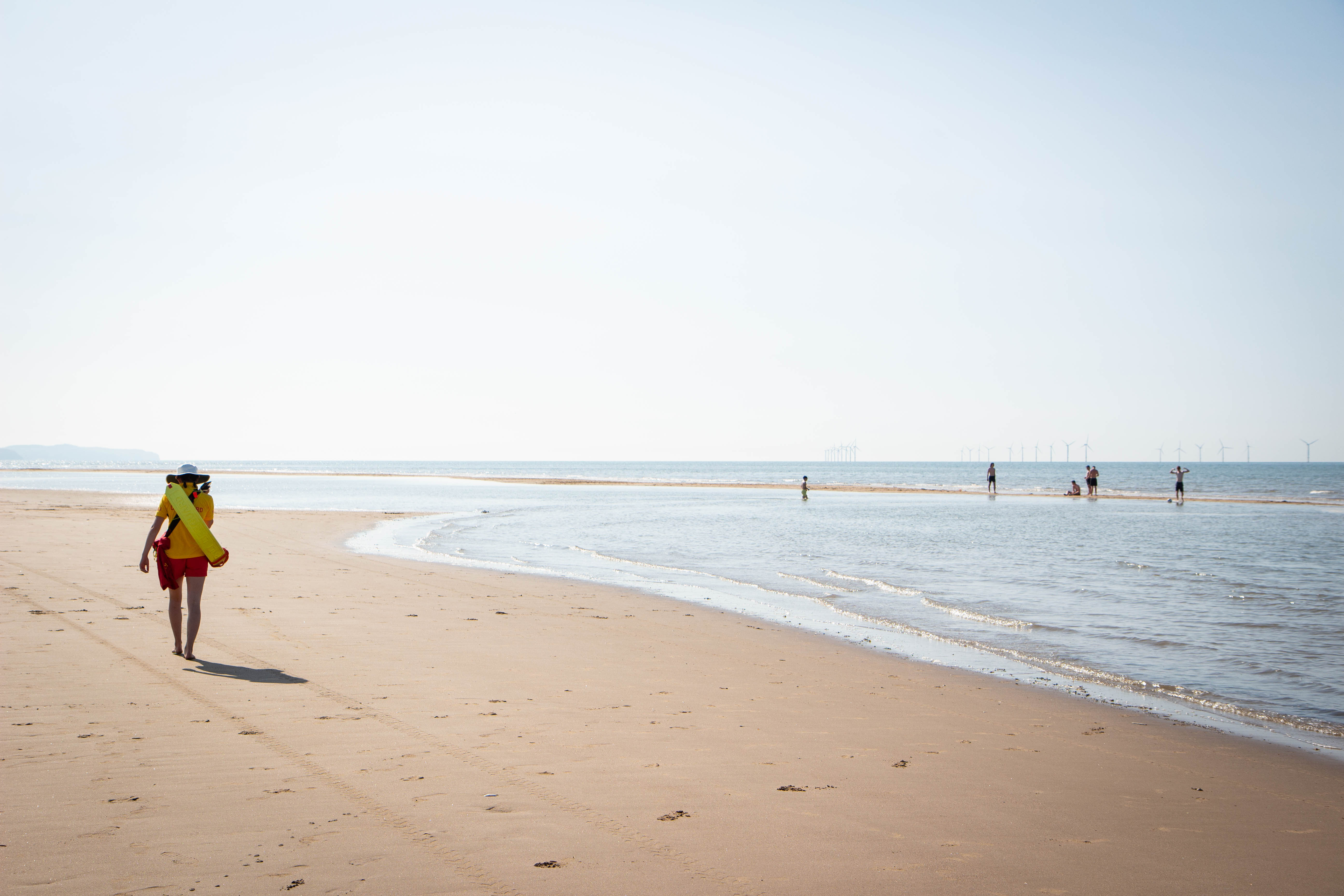 Landscape image of RNLI lifeguard patrolling the beach on a sunny day