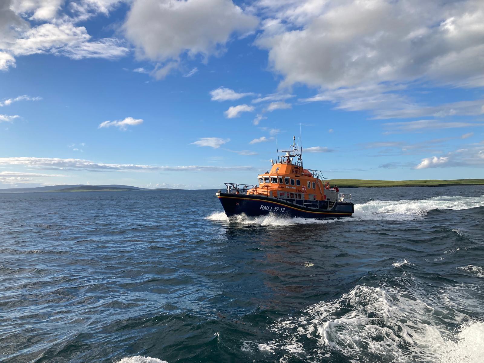 RNLB Margaret Foster making good speed towards Kirkwall Harbour in calm seas under a bright blue evening sky with high white clouds