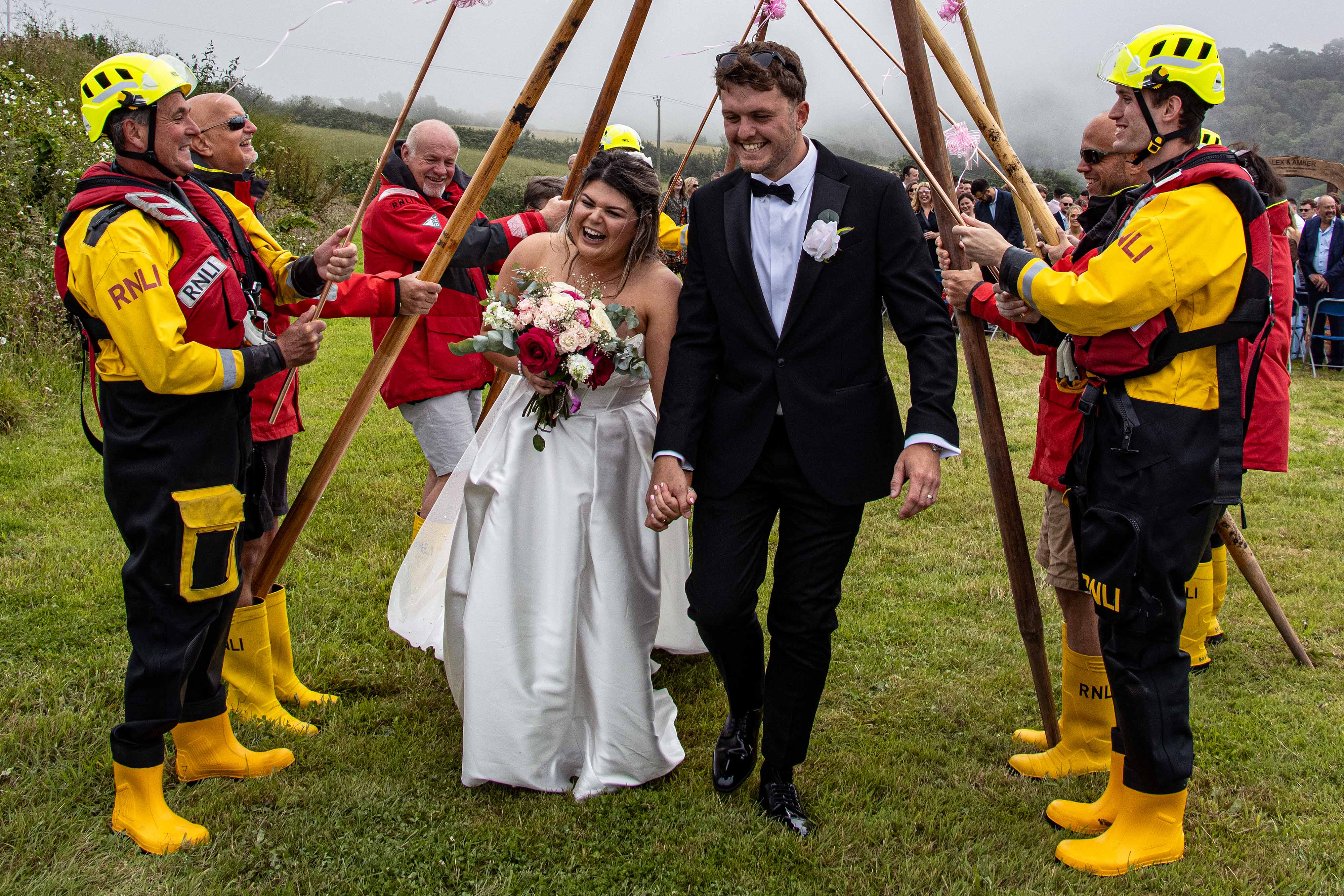 Amber and Alex Richardson walking through Looe RNLI’s yellow welly guard of honour after their marriage