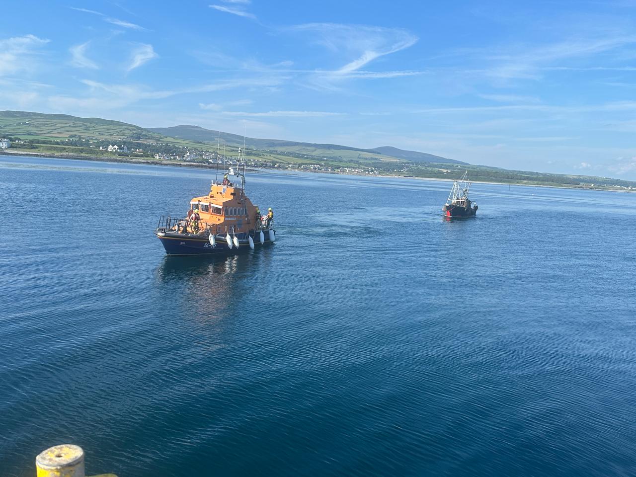 Port St Mary all weather lifeboat returning to Port St Mary towing the fishing boat. Hills of Isle of Man in background.