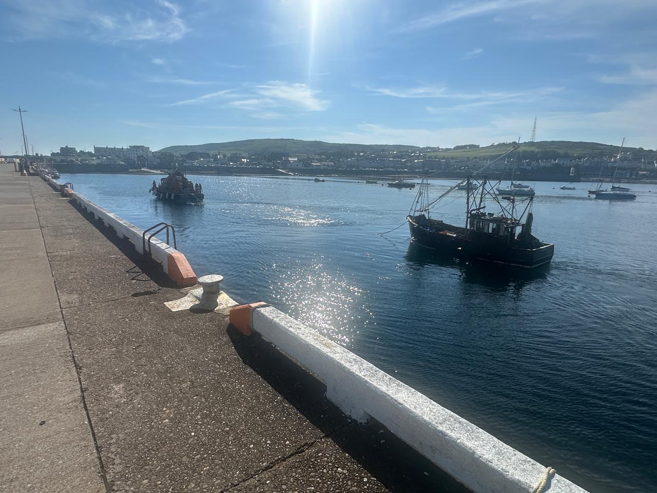Picture of lifeboat towing the fishing boat on a sunny day. Just pulling up alongside the breakwater.
