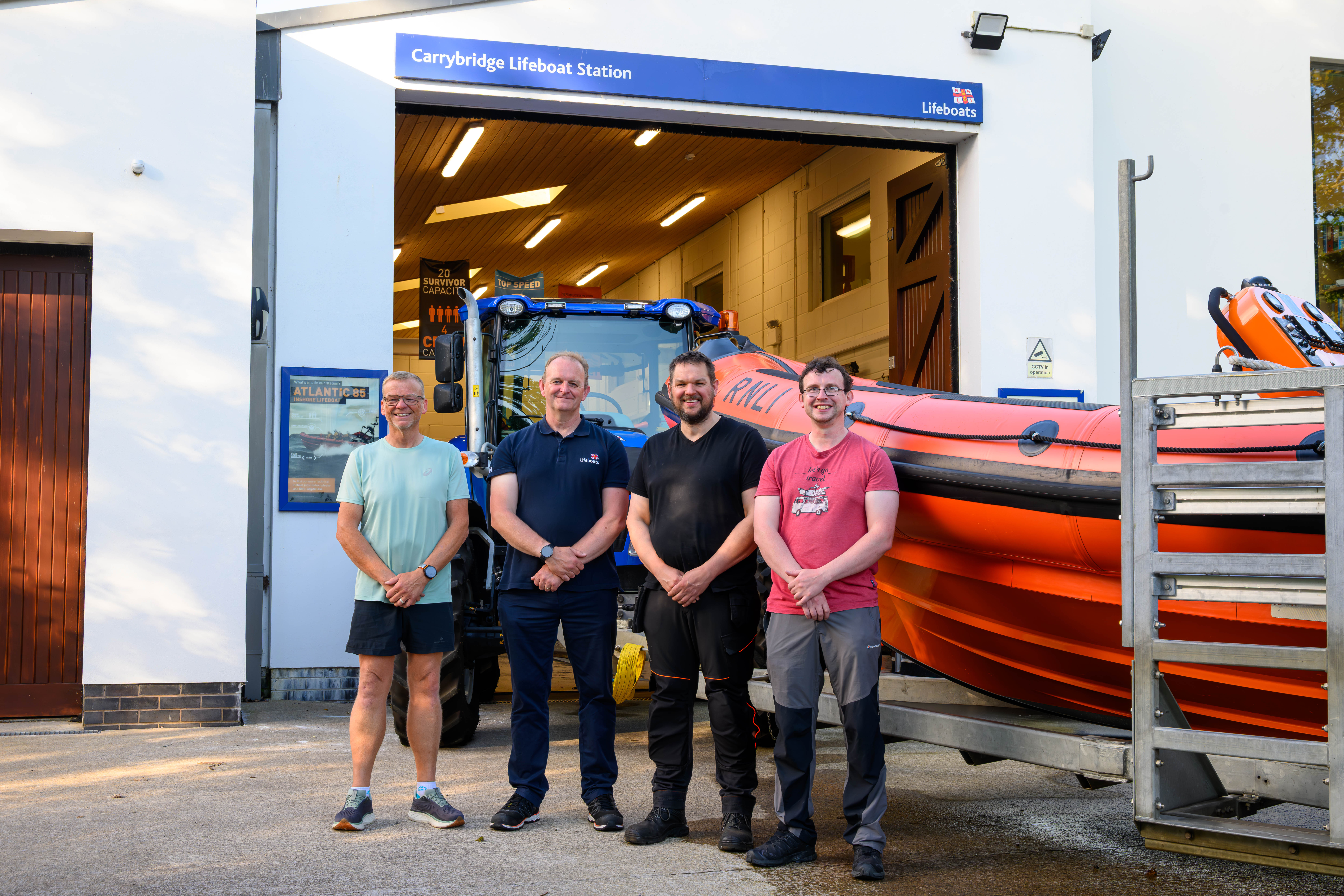 On the left of the photo is Carrybridge RNLI Helm, Thomas Graham, with Sean Ginnelly, Coastal Lifeboat Trainer, Simon Carson, Navigator and Colin Beacom, Navigator. Both Carrybridge RNLI B-Class lifeboat and Carrybridge Lifeboat Station are in the background of the image.