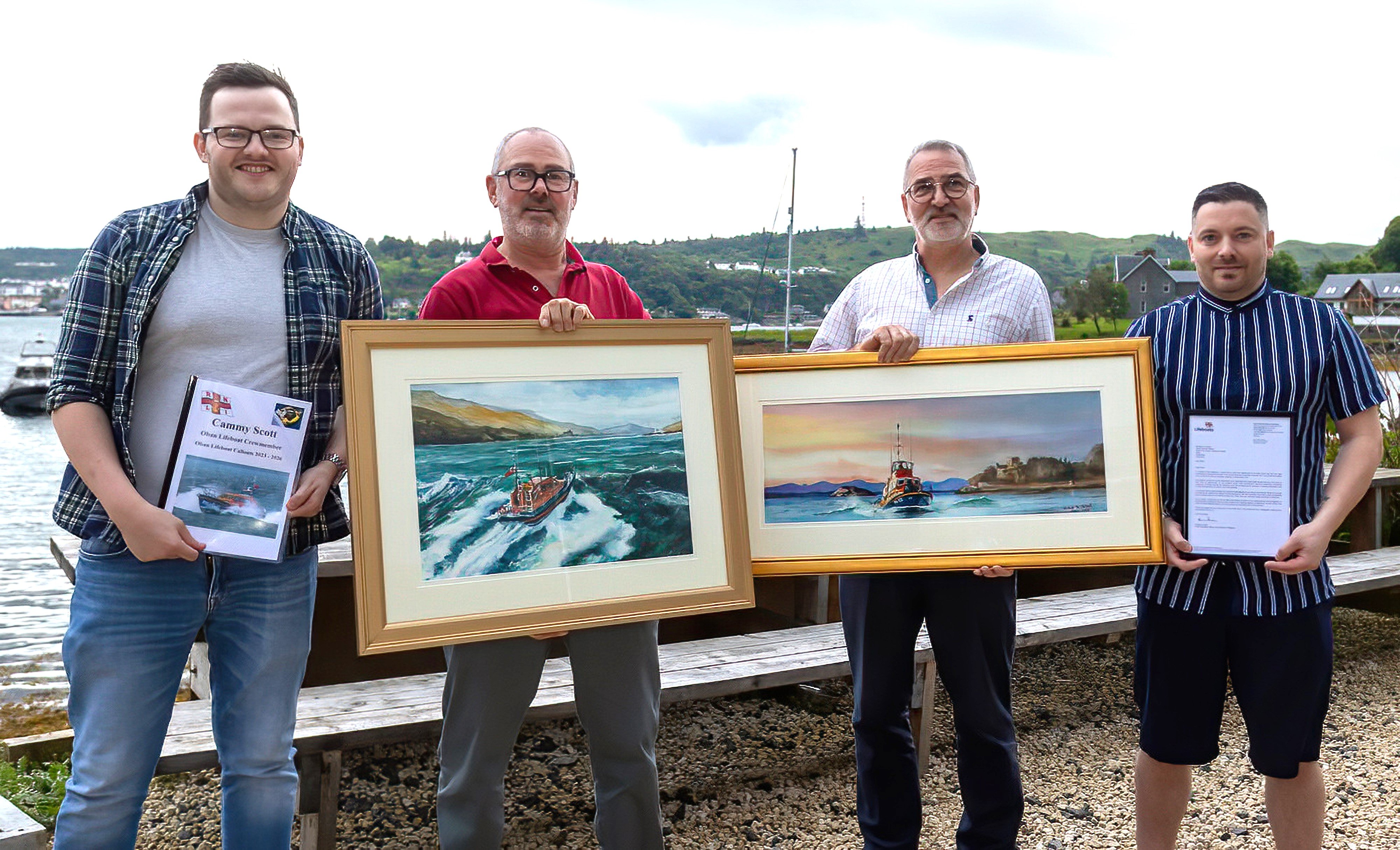 Four men stand holding certificates and paintings they have been presented by colleagues to mark their retirementst.
