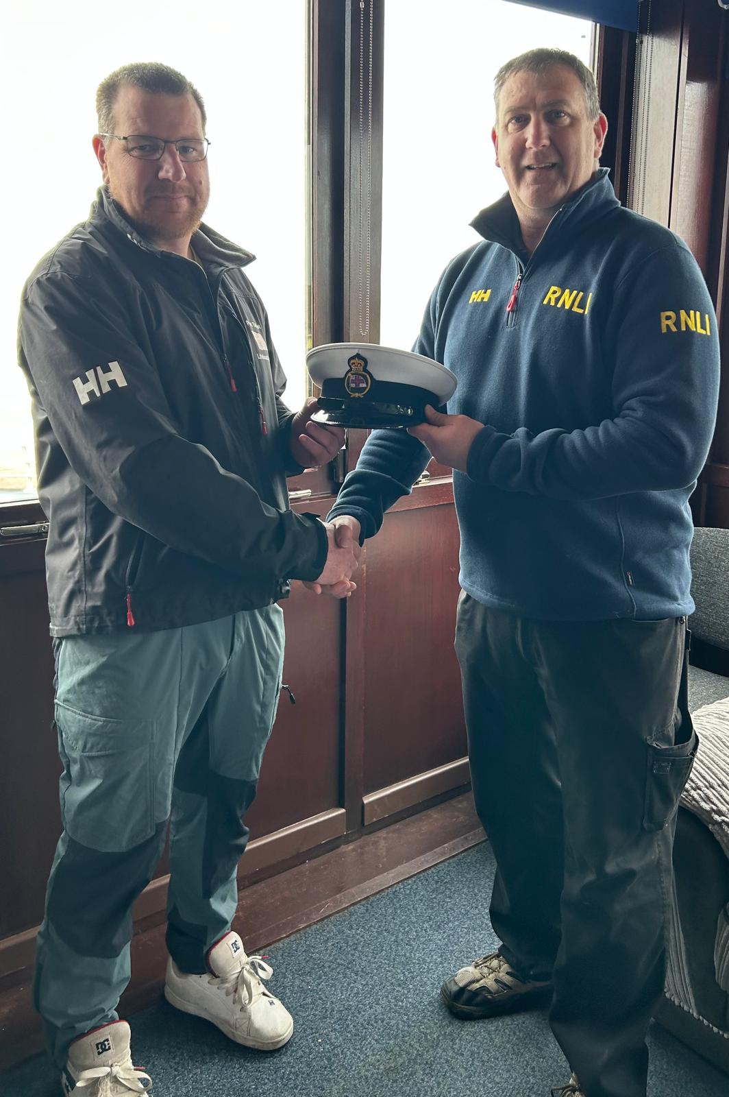 Gareth Kehoe and Paul Taylor shaking hands, with Paul handing Gareth his helm cap.

