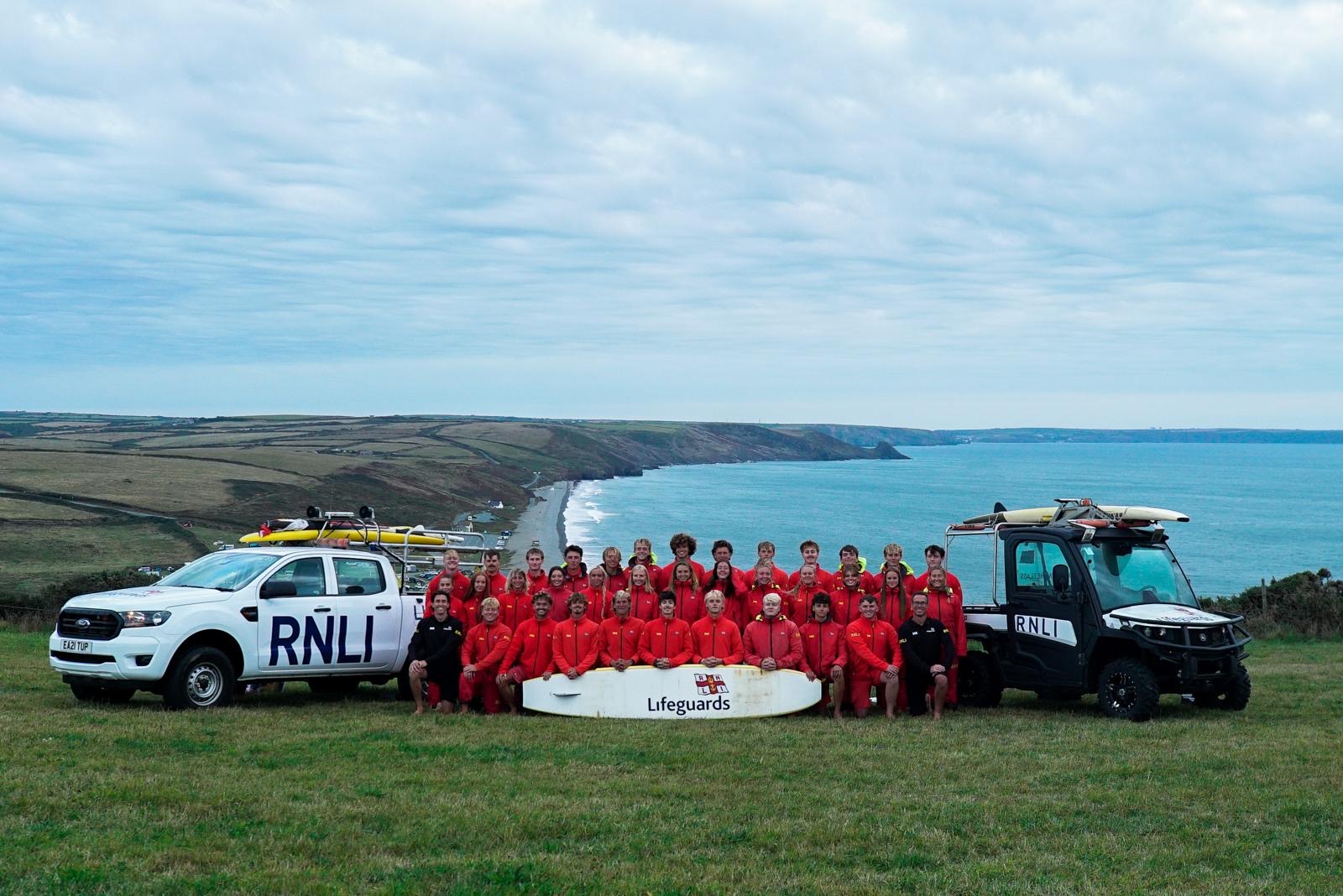 RNLI lifeguard team stood in front of coastline in uniform 