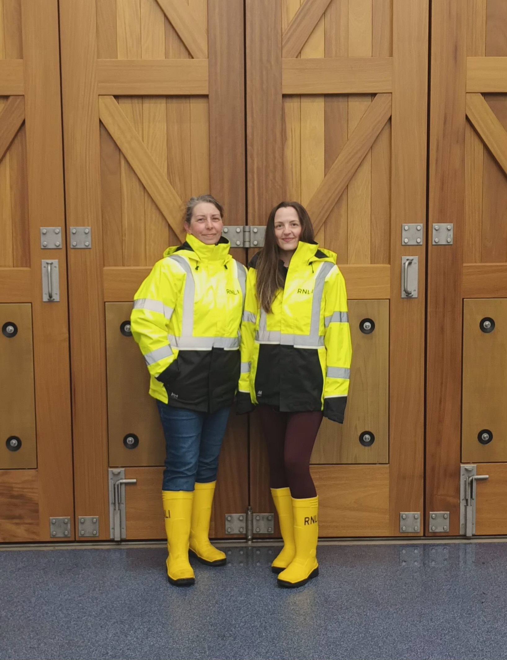 Shore crew volunteers in yellow jackets and boots stood inside the boat hall in front of the large wooden storm doors
