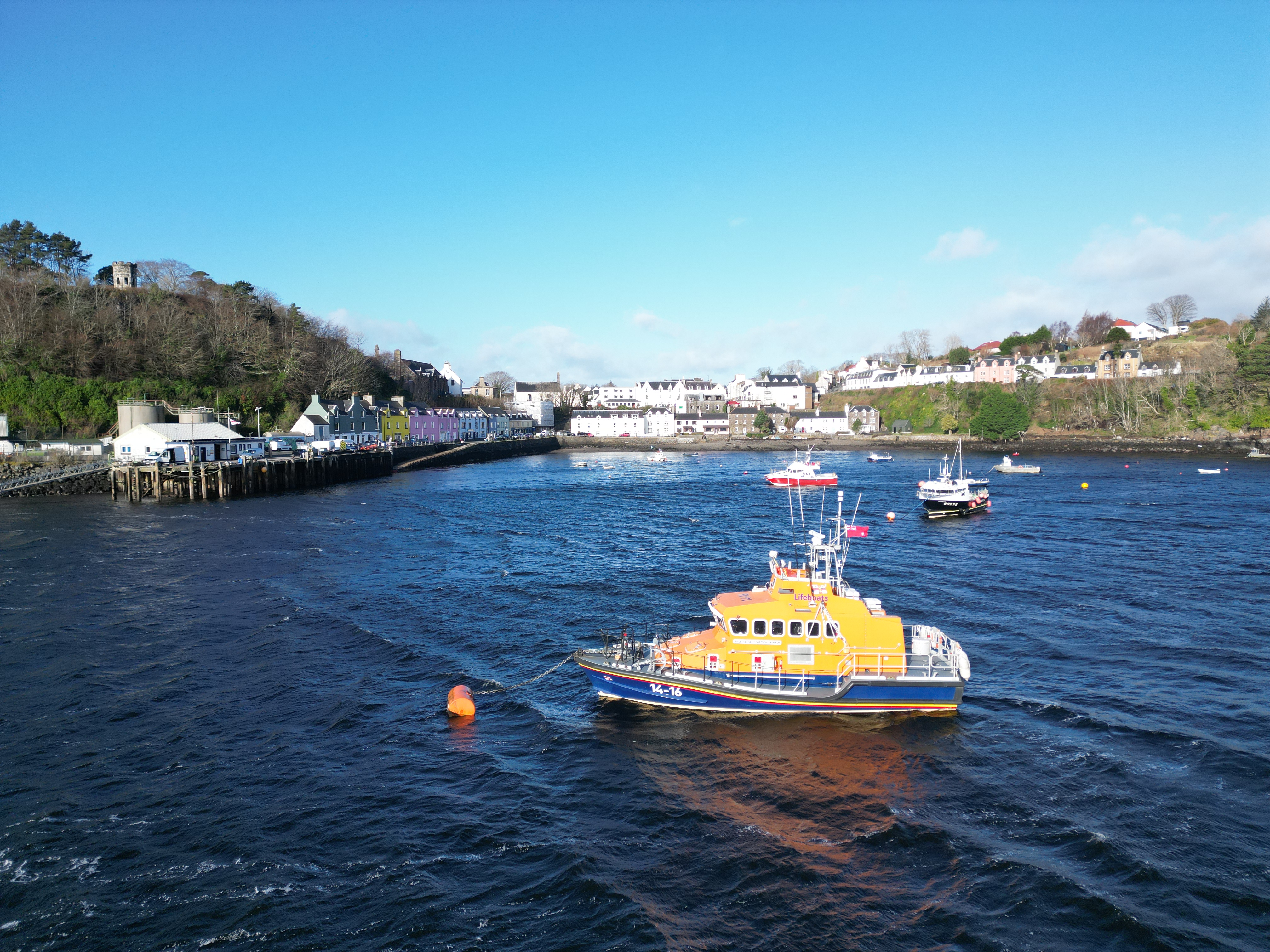 Portree RNLI lifeboat on the mooring in Portree bay, with the multicoloured buildings on the pier behind.