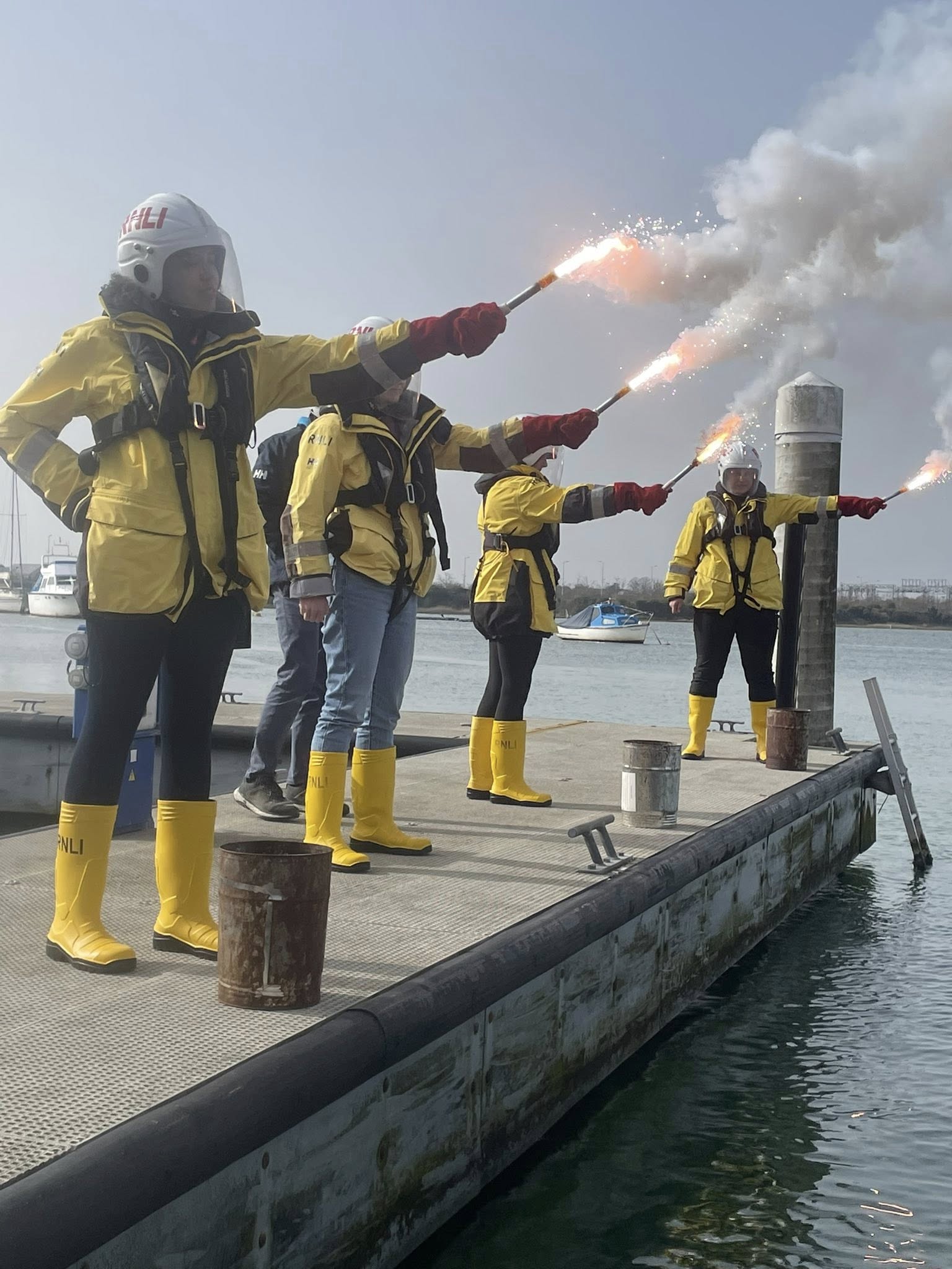 RNLI crew members stand on Poole Harbour with flares as part of their training