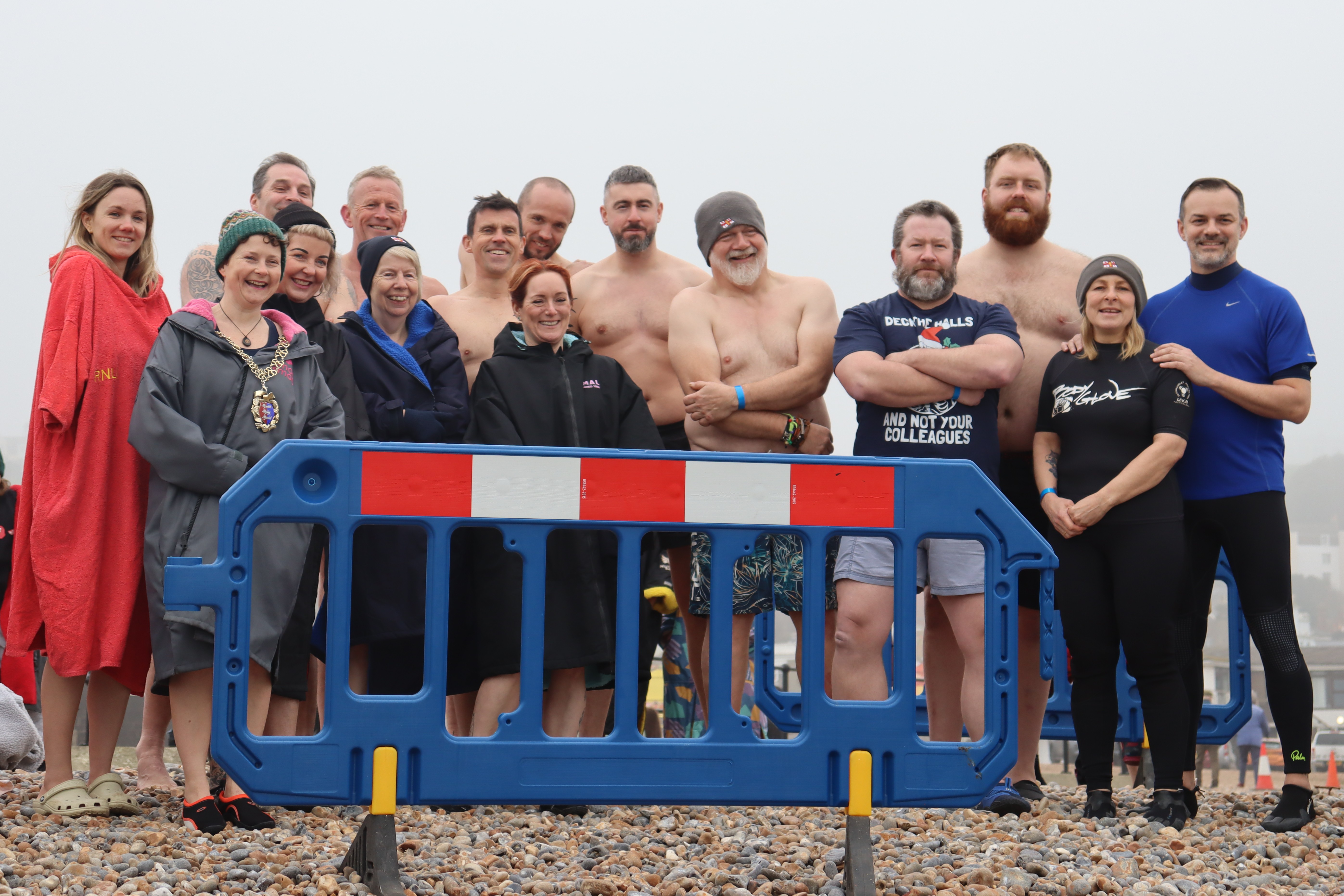 A group of RNLI crew in beachwear, and the mayor of Hastings in her chain, on the beach