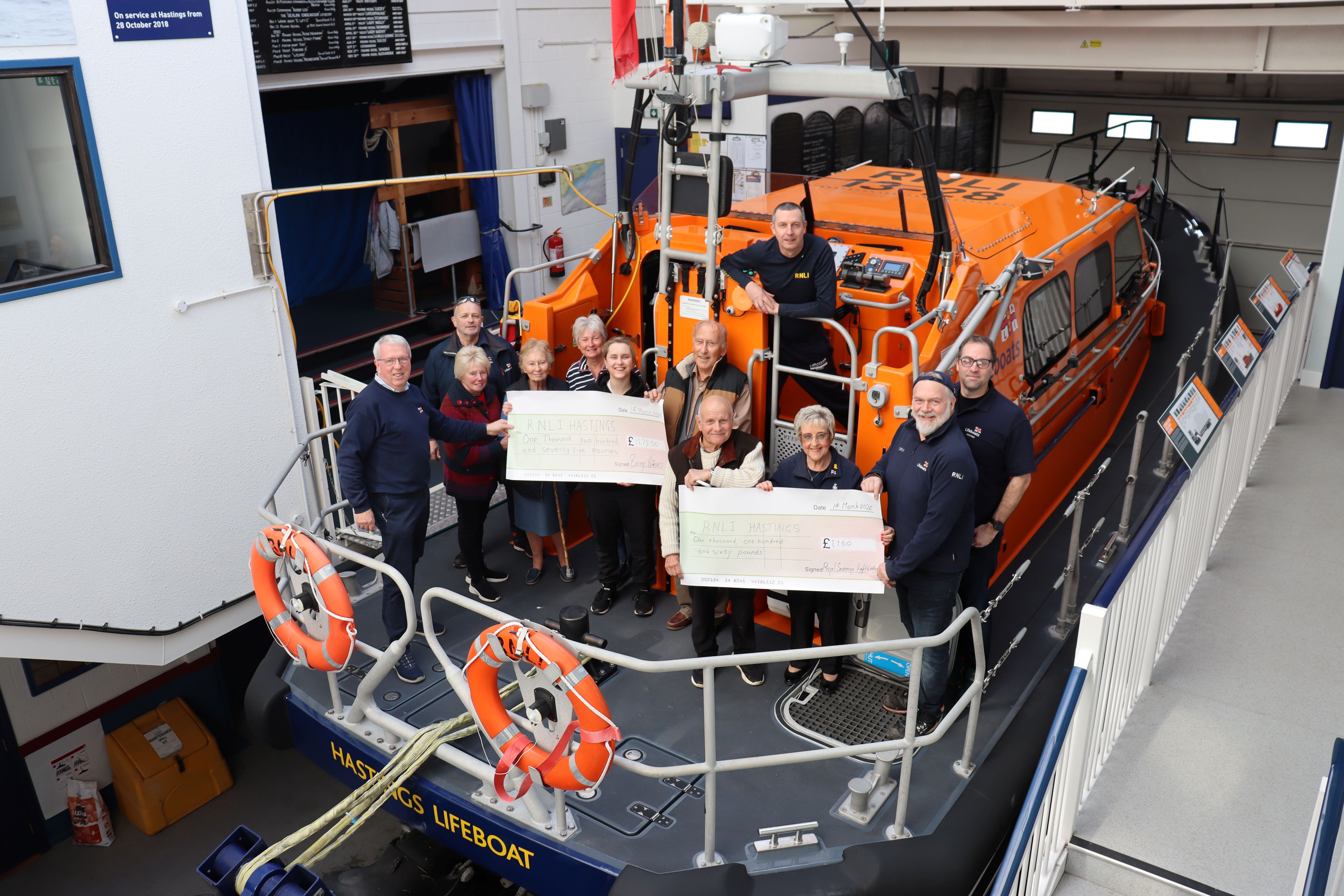 A group of donors presenting two large cheques on board Hastings lifeboat, surrounded by RNLI crew and volunteers