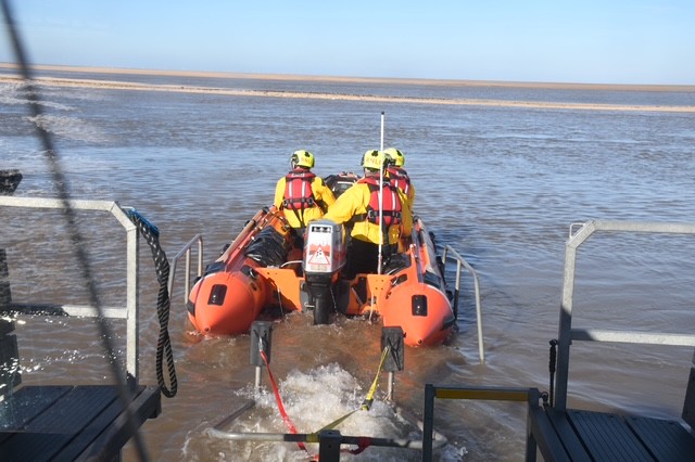 Wells RNLI D class lifeboat launching with a crew of three in full RNLI branded inshore lifeboat kit sunny weather and blue skies