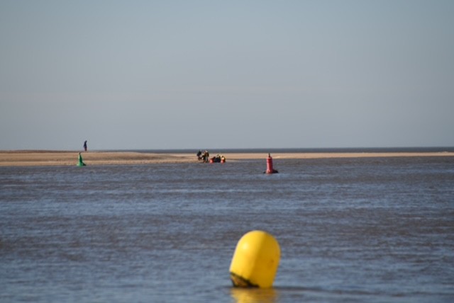 Wells RNLI D class lifeboat assisting people cut of by the tide blue skies and open sea and a yellow buoy in the foreground