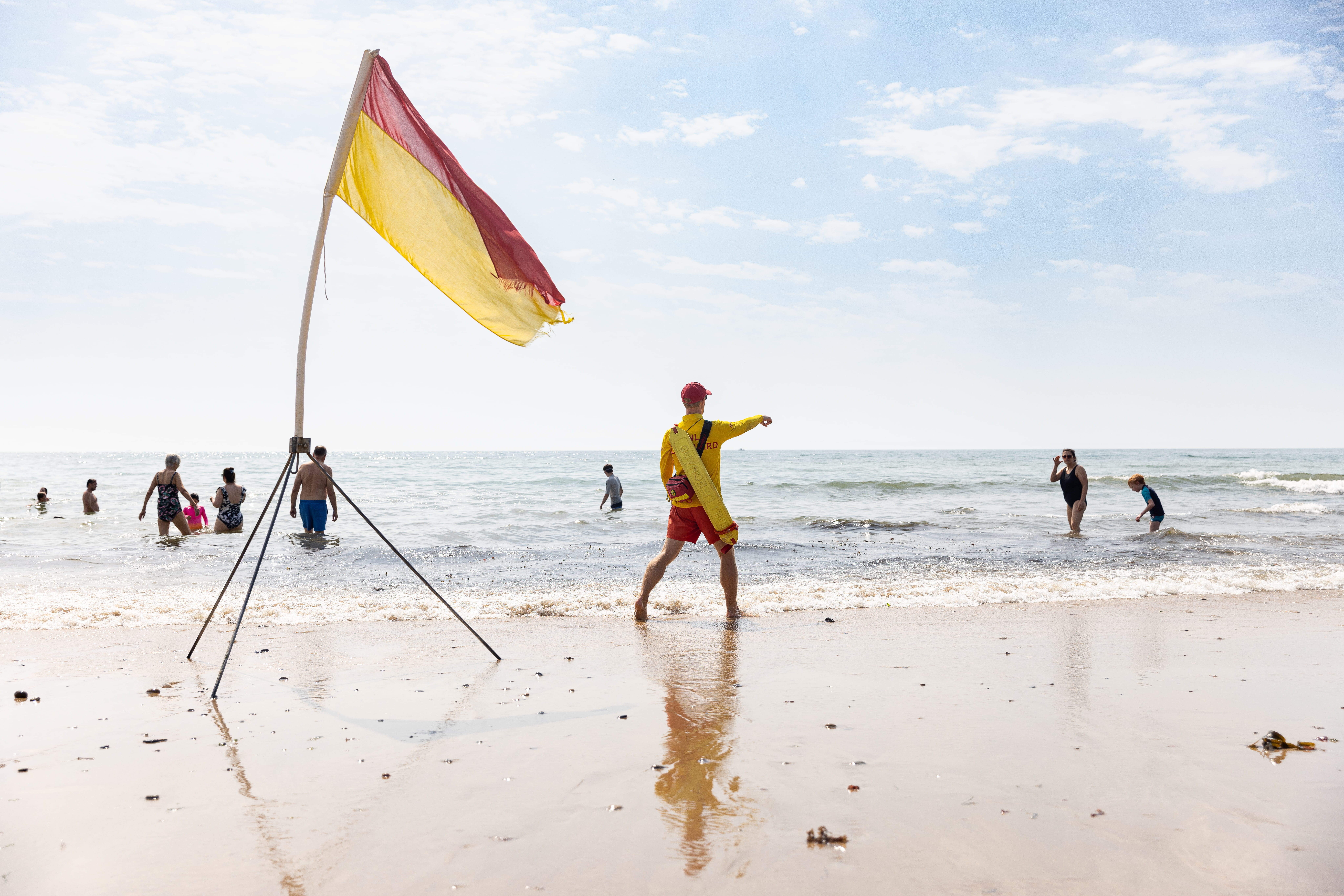 RNLI senior lifeguard Tom Henderson moving a red and yellow flag at at Langland Bay, South Wales.