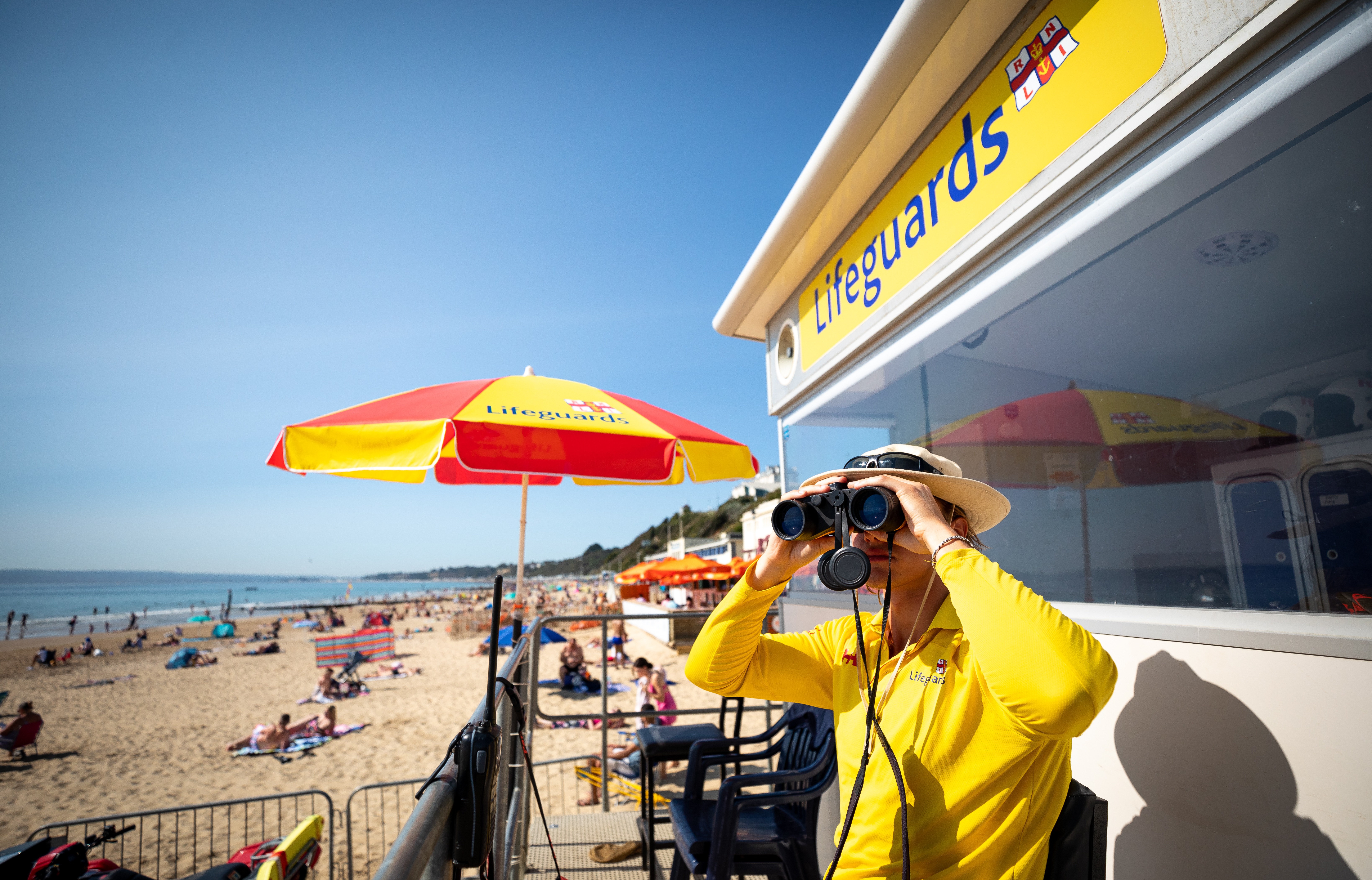 RNLI lifeguard Adam Franklin monitoring the beach at Bournemouth from the lifeguard tower and using a pair of binoculars.