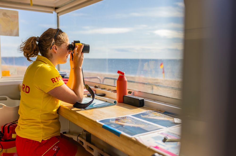 RNLI lifeguard looking through binoculars out the lifeguard unit