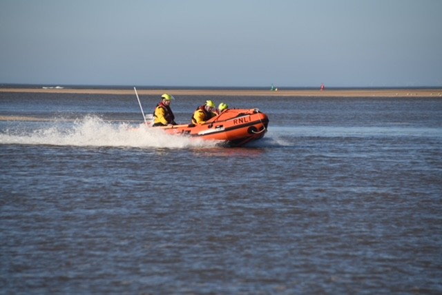 Wells RNLI D class lifeboat launching with a crew of three in full RNLI branded inshore lifeboat kit sunny weather and blue skies