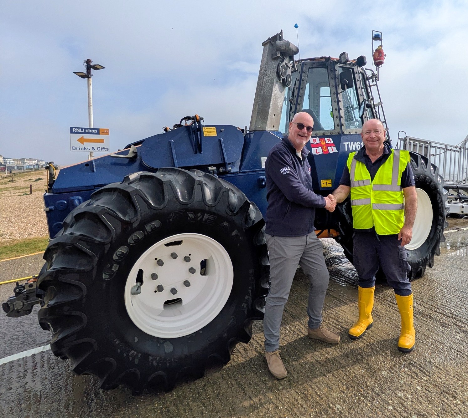 Two smiling RNLI volunteers shaking hands infront of a large tractor