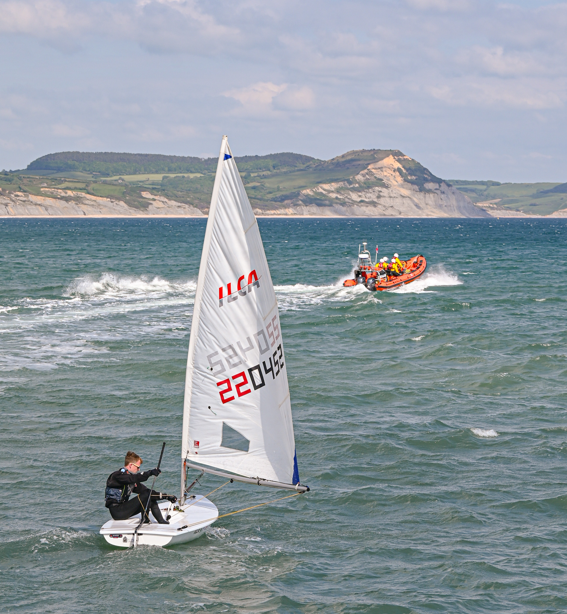 Orange lifeboat at sea followed bby white sailing dinghy