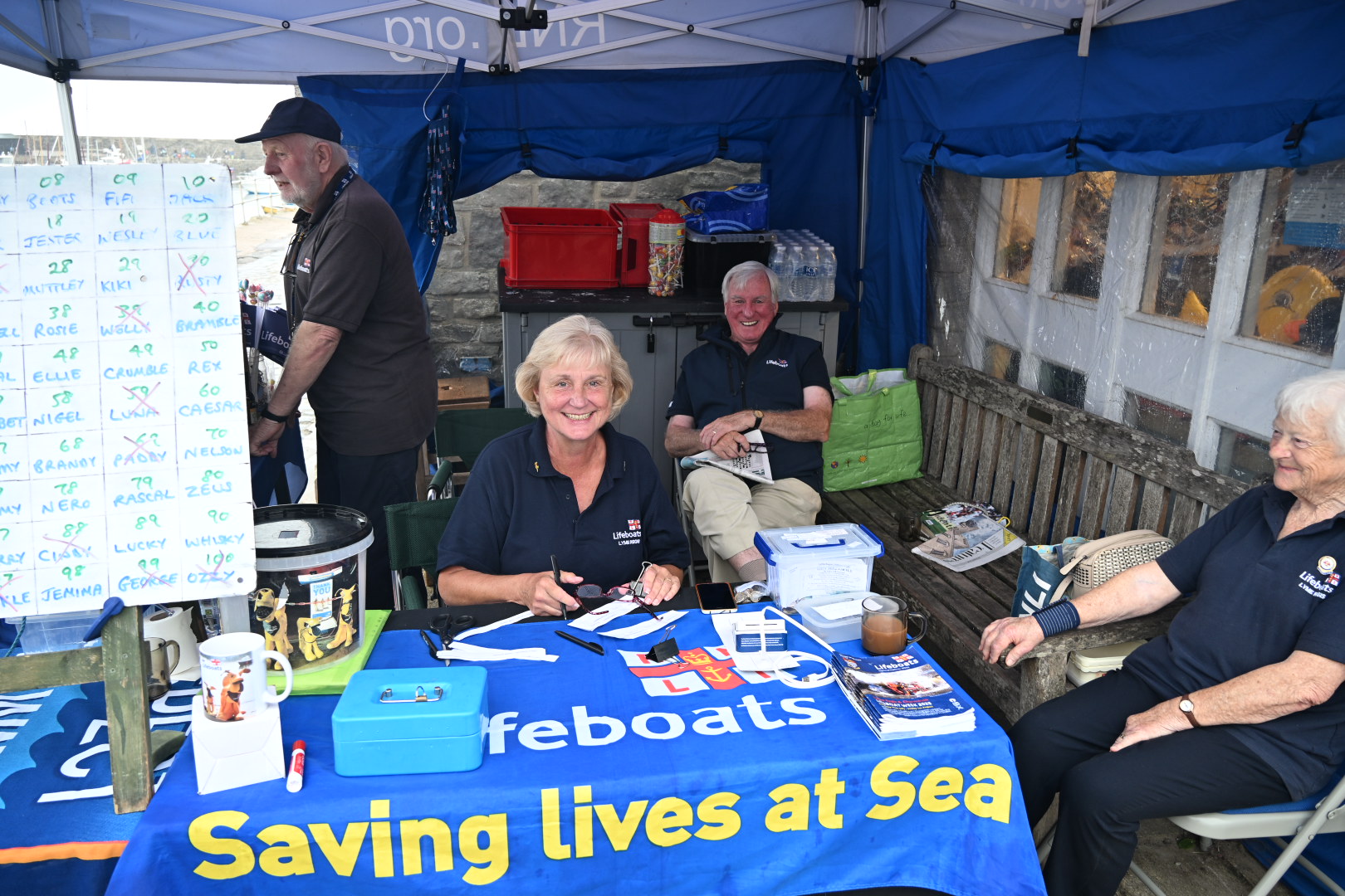 People in blue tops sat behind saving lives at sea sign on table