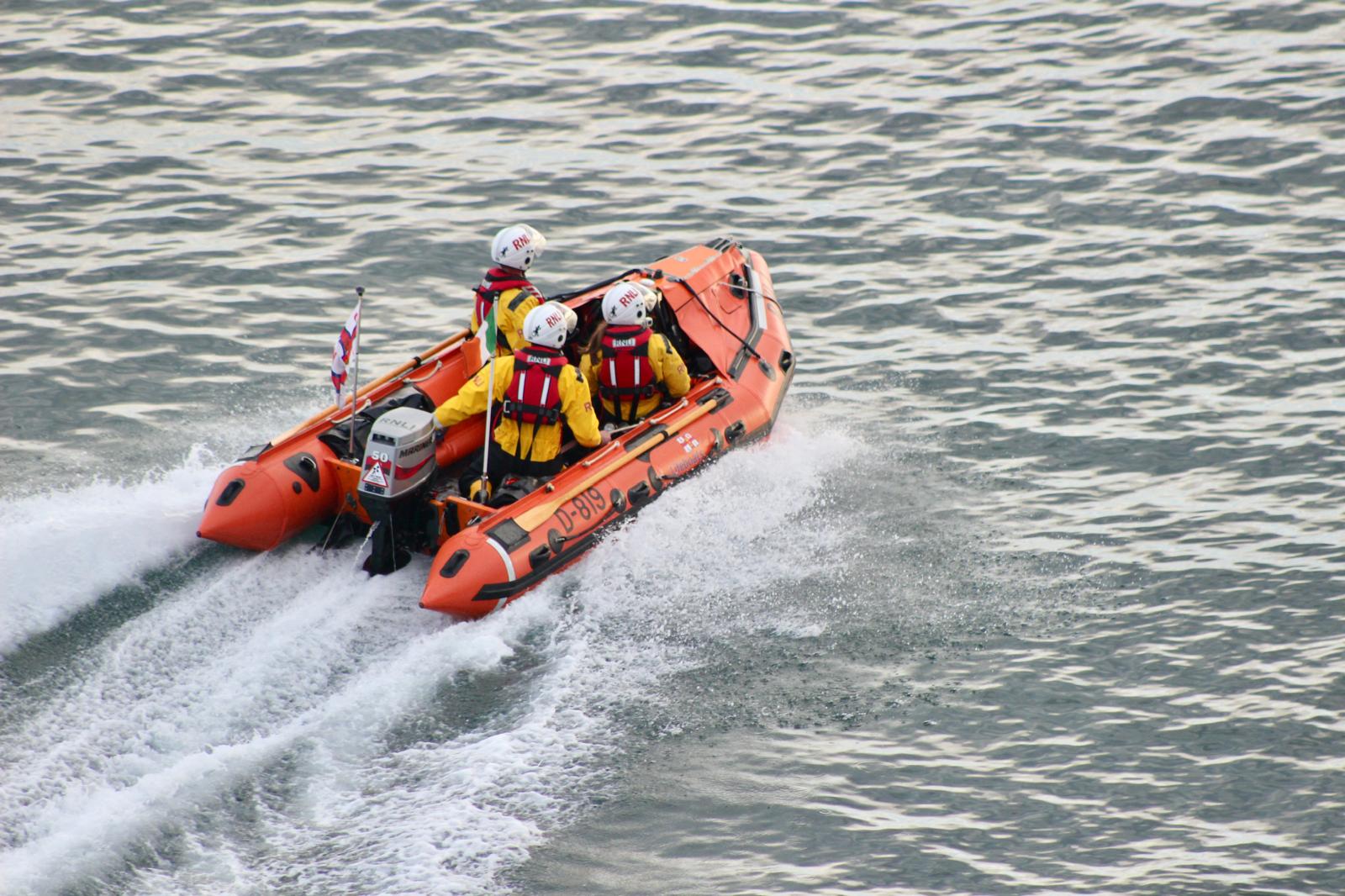 The attached photo shows Fethard RNLI D-class Naomh Dubhán underway at sea.The orange lifeboat is travelling away from the photographer. There are 3 crew members on board dressed in yellow drysuits and red lifejackets.