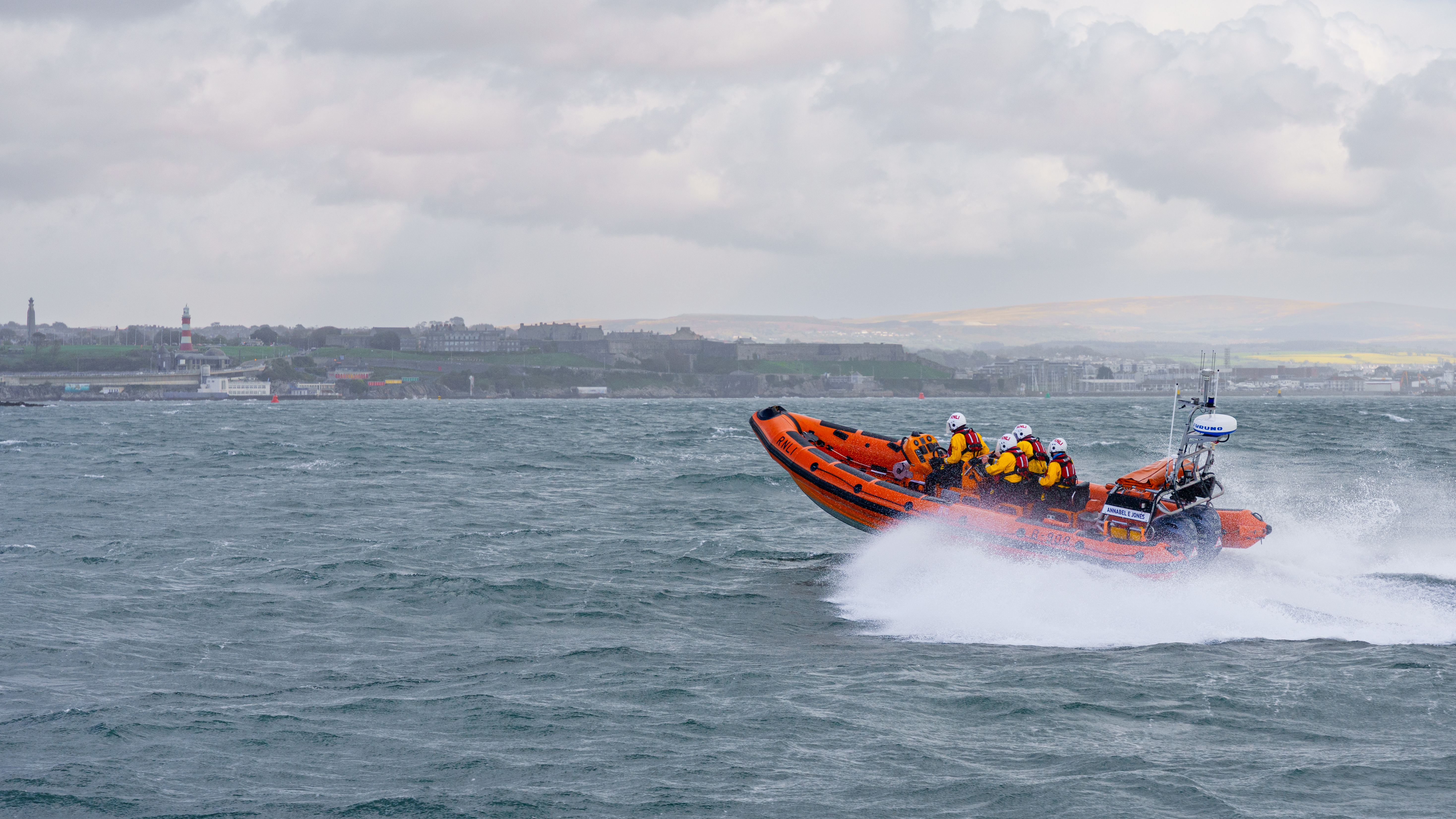 Inshore Lifeboat driving at speed across water with Plymouth in the background
