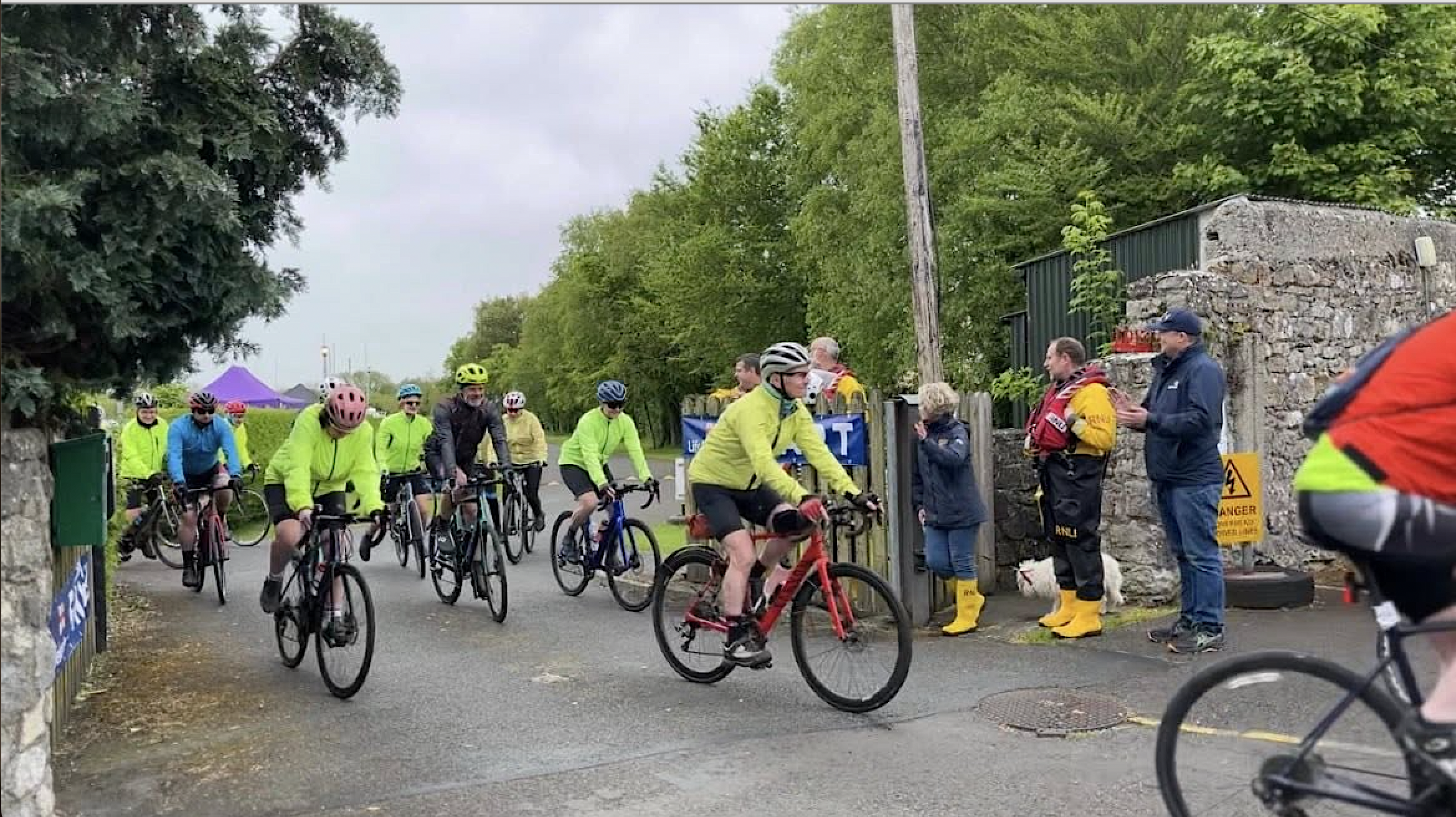 Cyclists setting out through the gates of Lough Derg Yacht Club, with volunteers from Lough Derg RNLI standing by and cheering them on