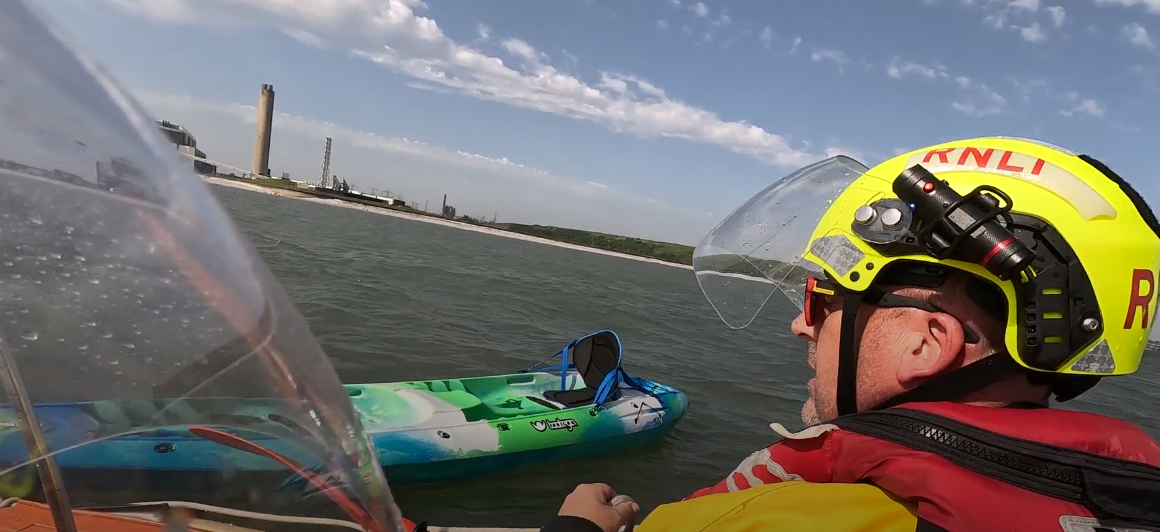 A blue and green kayak floats beside the RNLI lifeboat with the coastline with Aberthaw power station visible in the distance.
