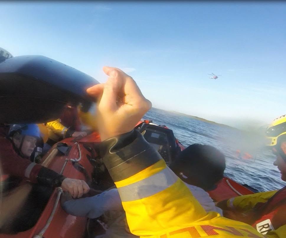 A shot of crew members in the foreground aboard D-Class lifeboat, visible in the distance is Coastguard Rescue helicopter 189.