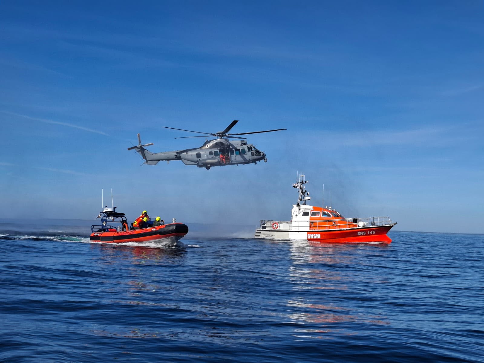 A helicopter hovers above two boats.