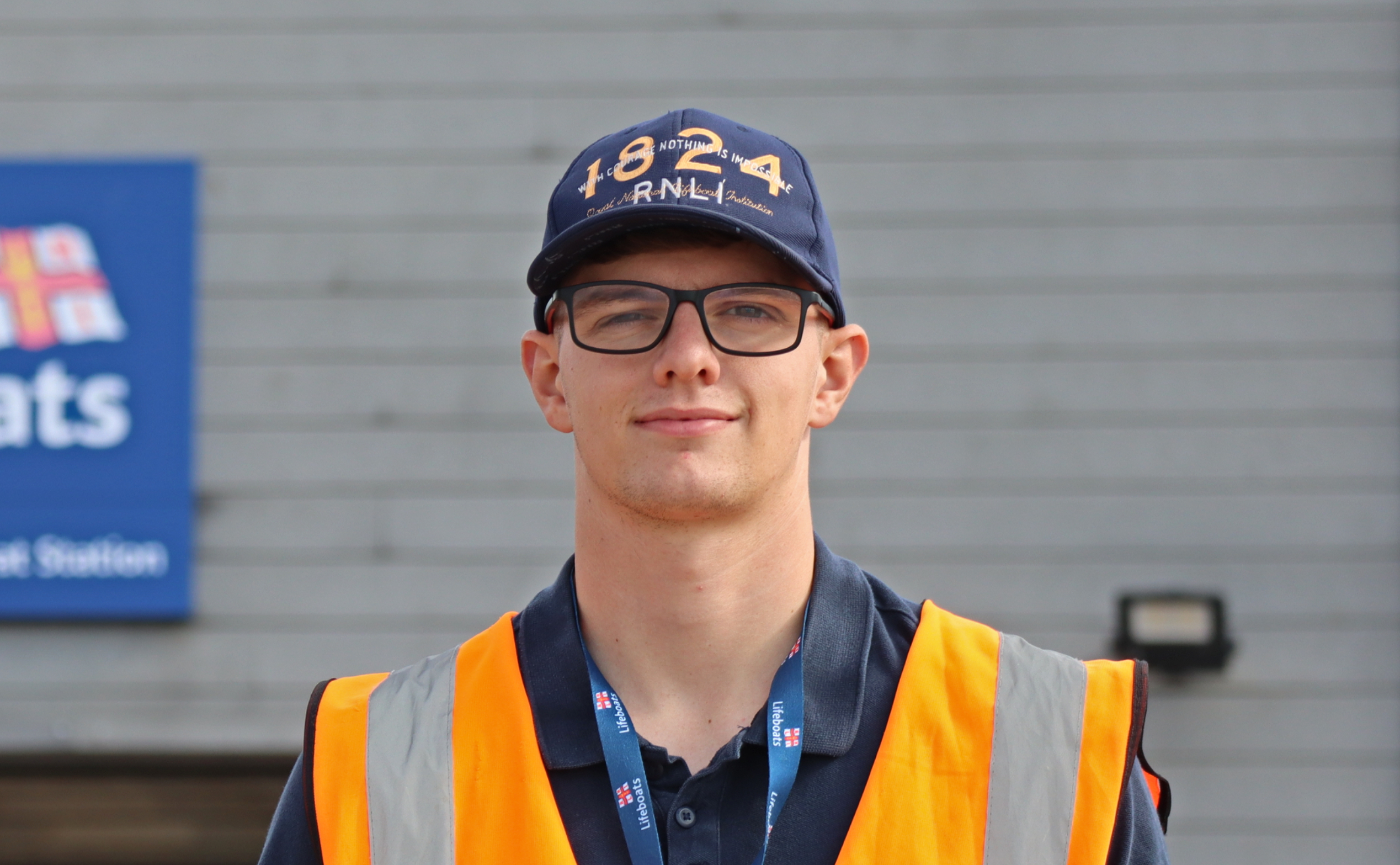 A head and shoulders shot of Josh Bruford. Josh, wearing an orange Head Launcher hi-vis and an RNLI baseball cap, looks straight at the camera
