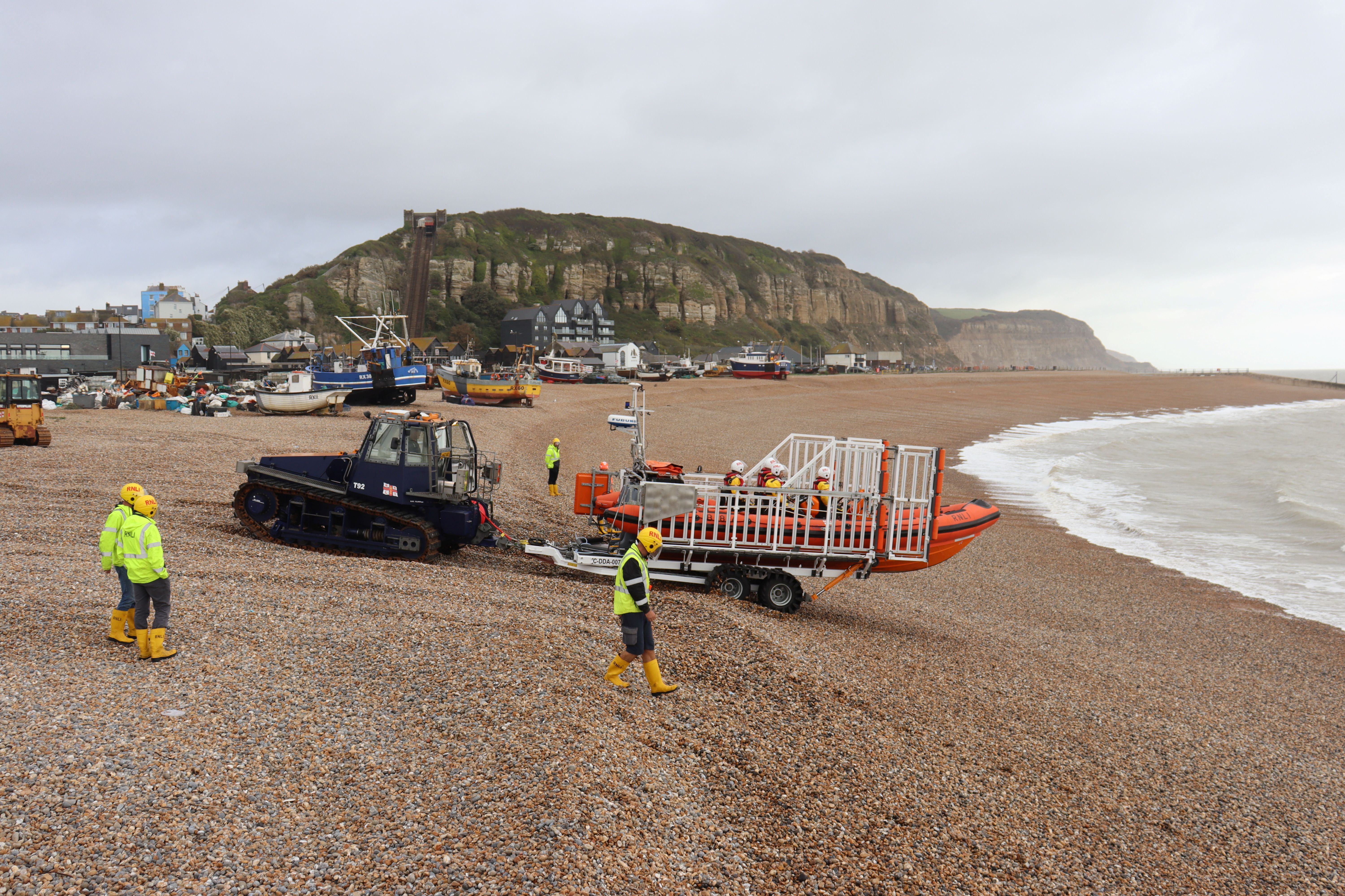 The lifeboat being pushed by the tractor, against a backdrop of Hastings fishing fleet