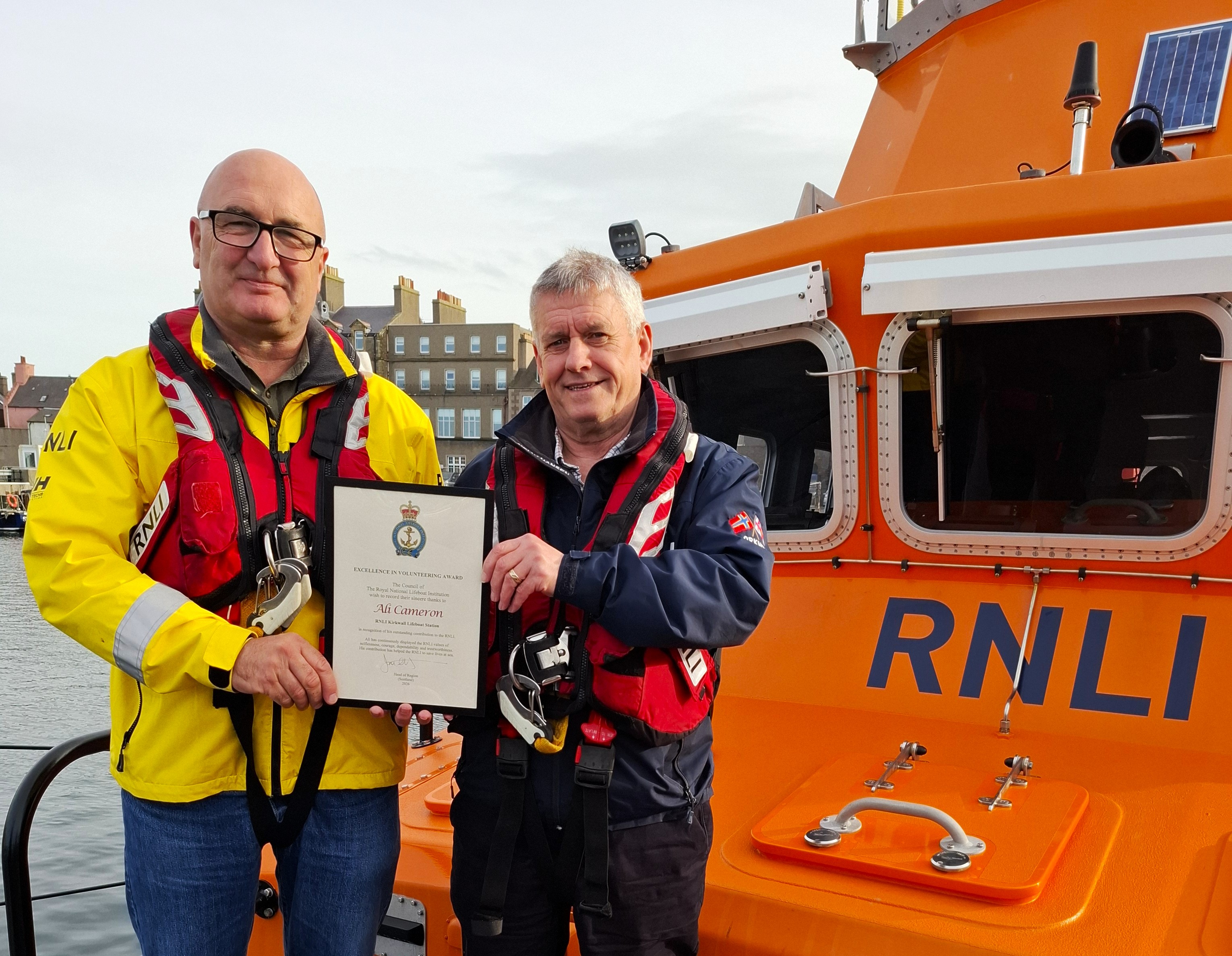 Two men on board an RNLI lifeboat. One man is presenting the other with an award.