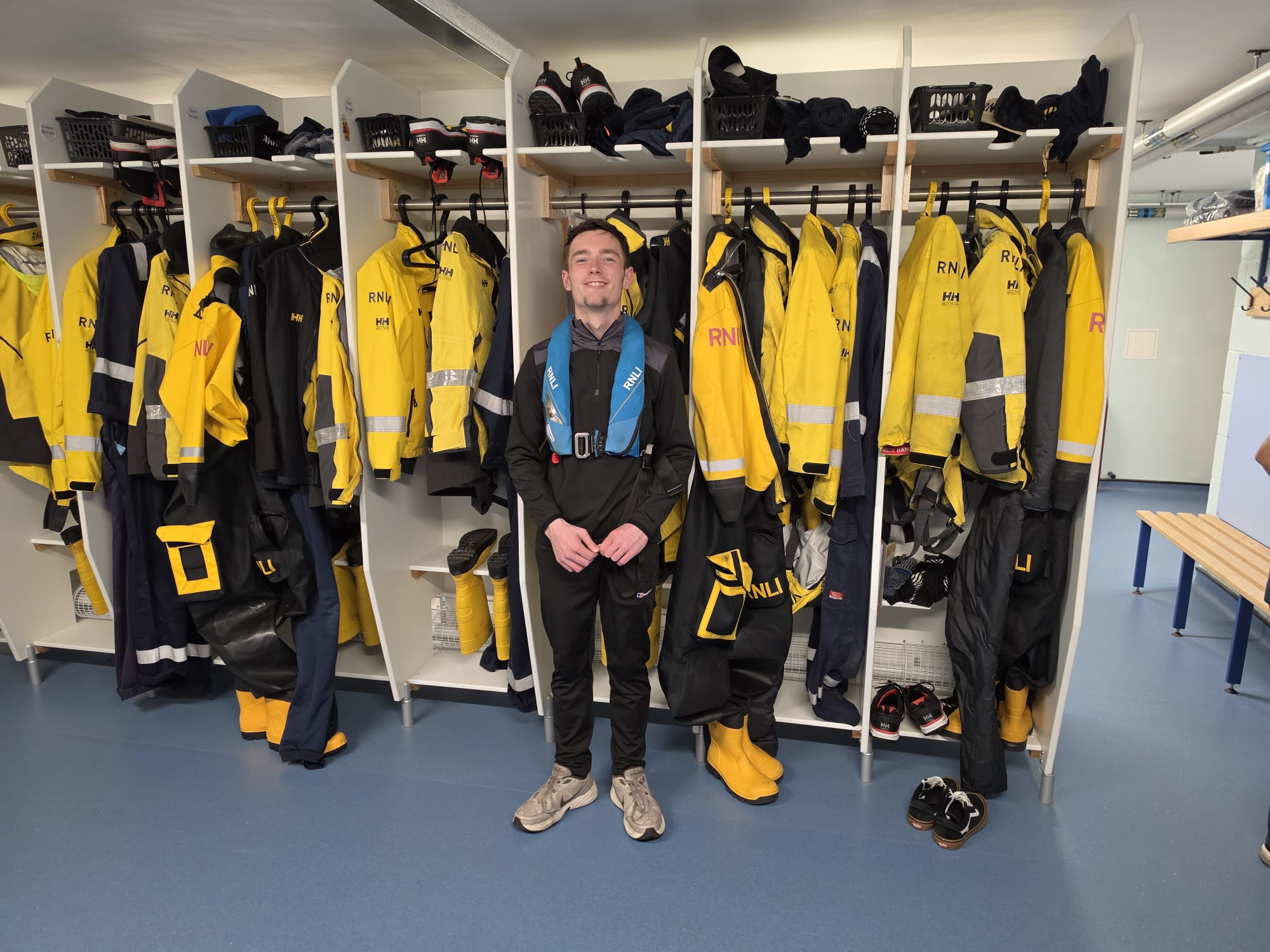 A young man standing in front of the RNLI yellow kit in the room where the volunteer crew kit up